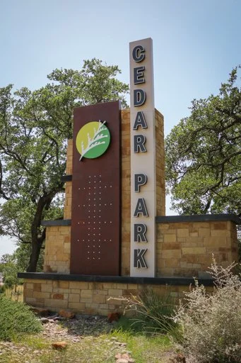 Sign for Cedar Park with a green leaf logo and tall vertical lettering.