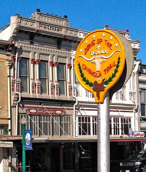 Sign for Singing Up the Texas Longhorn Trail in front of a historic building with decorative architecture.