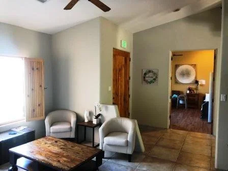 Living room with beige chairs, a wooden coffee table, and a wall with a wooden door and a window with blinds.