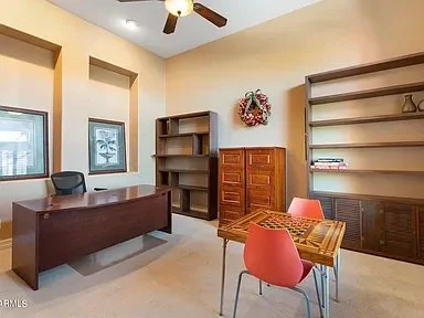 Office space with a desk, two chairs, a bookshelf, a cabinet, and wall art with a ceiling fan