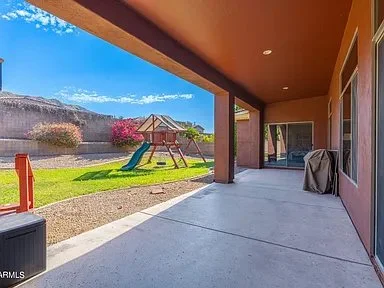 Covered patio area overlooking a backyard with a playground set and a mountain in the background.