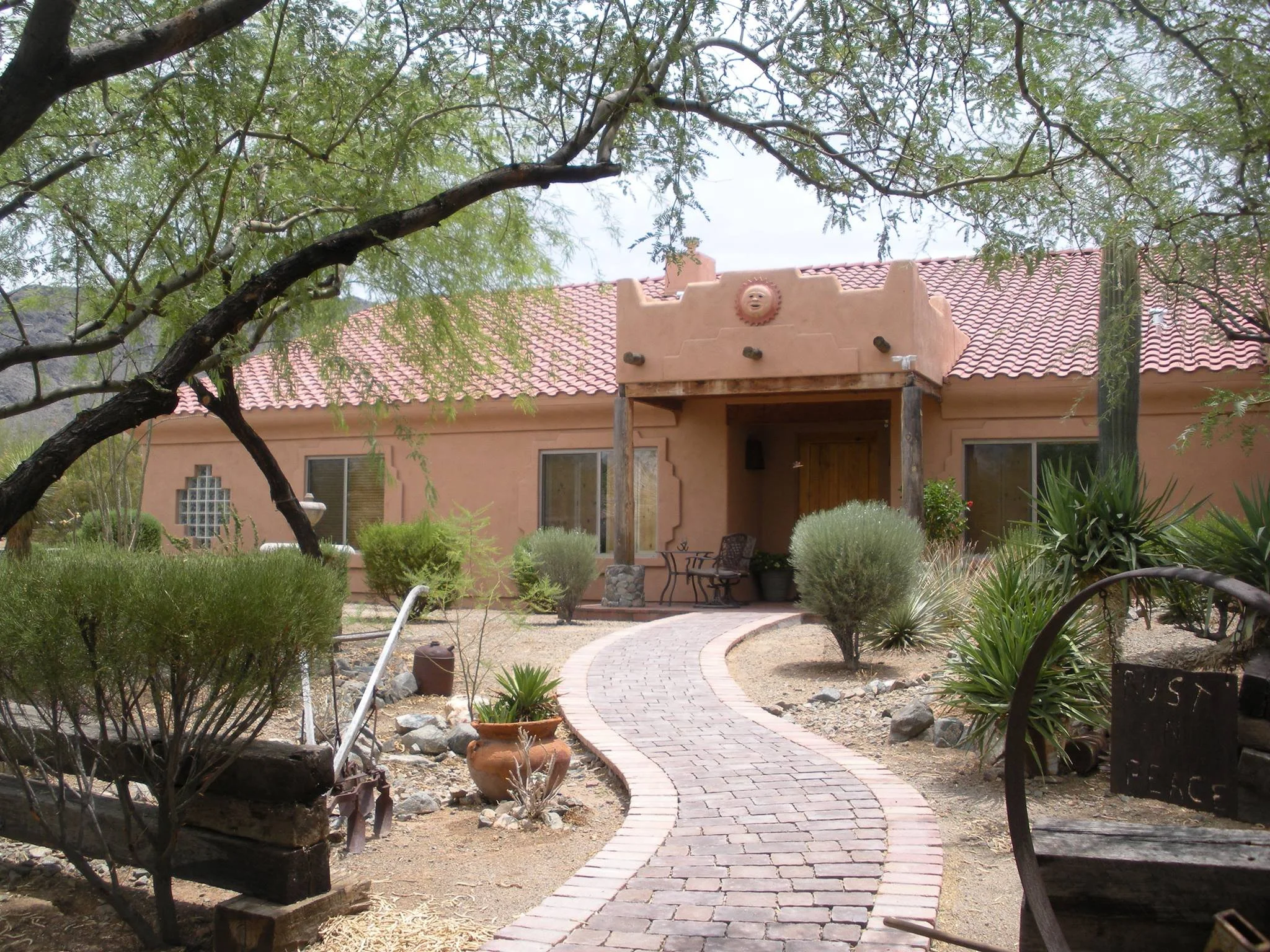A Southwestern-style house with a red tile roof, surrounded by desert plants and a curved brick pathway leading to the front porch.