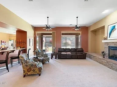 Living room with a brown sofa, armchair, and fireplace, open to the kitchen area.