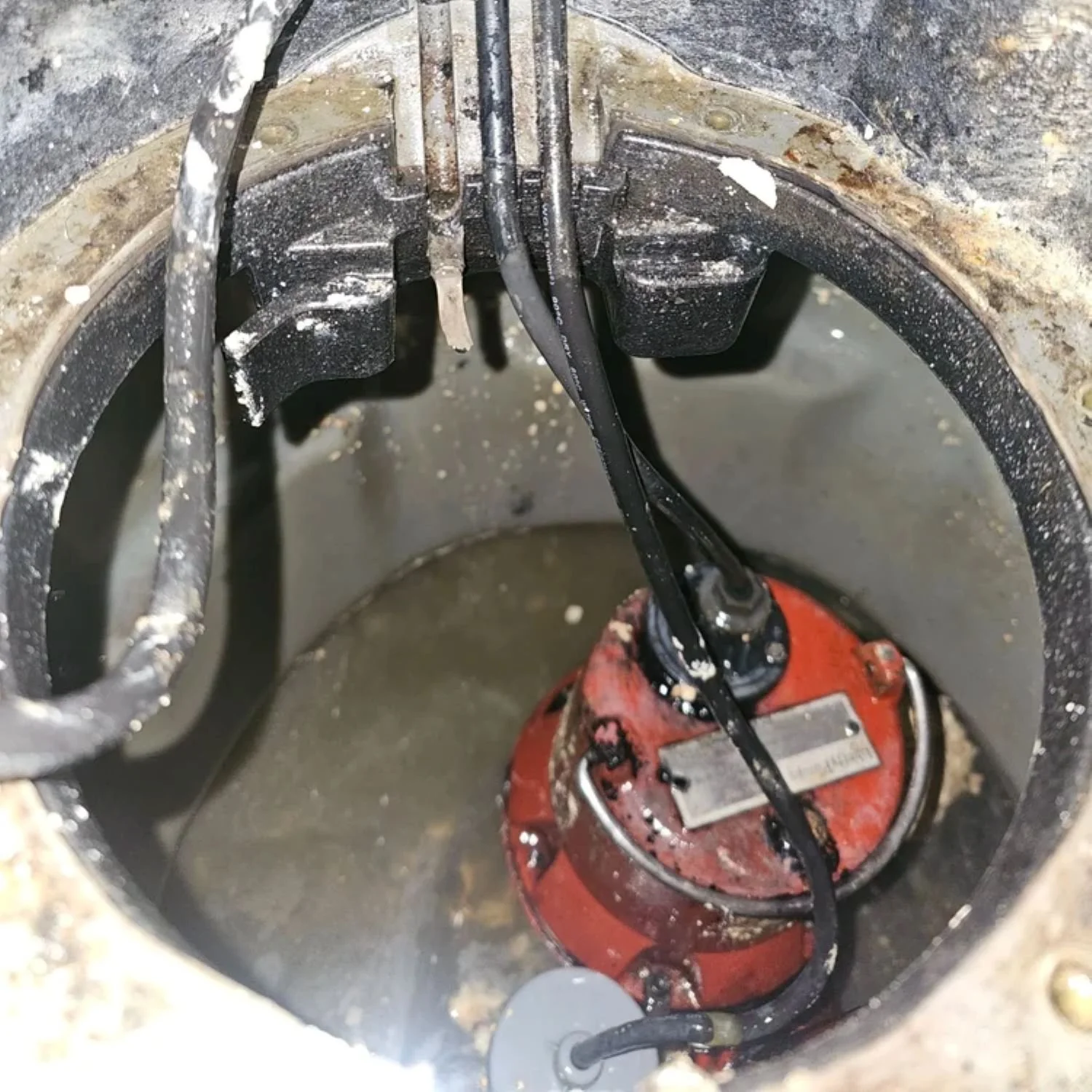An electric motor submerged in a sump pit with plumbing pipes and wires connected to it, possibly part of a sump pump system.