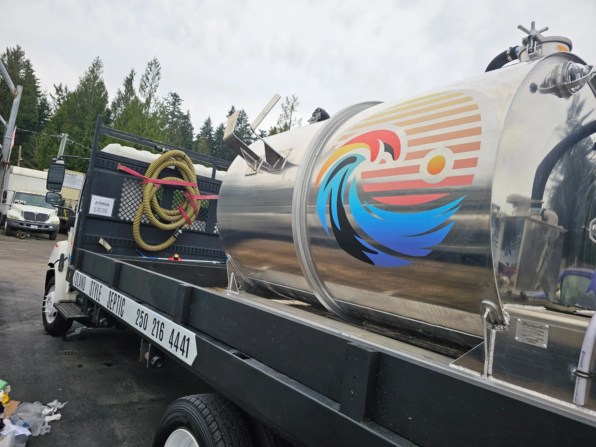 A septic truck with a colorful logo featuring a wave, sun, and sunset.