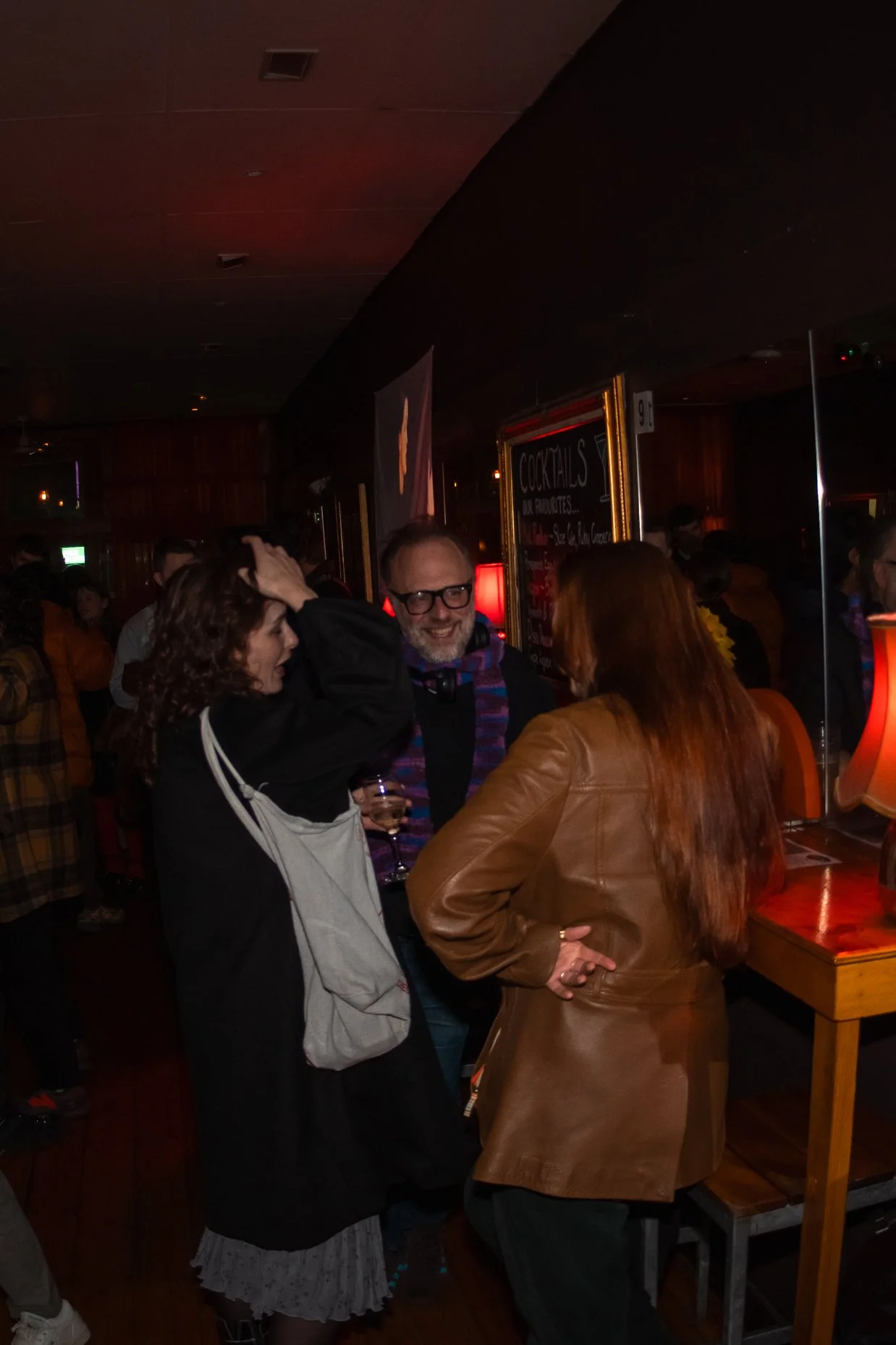 People socializing in a dimly lit bar or club, with some holding drinks and engaging in conversation.