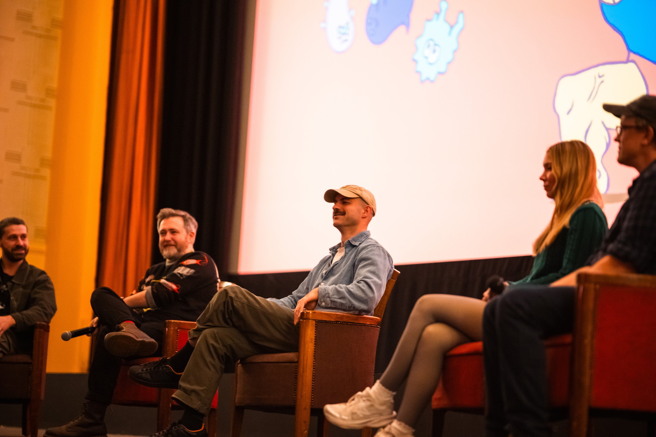 A panel of six people sitting on stage in front of a large screen displaying colorful animated cartoon characters.