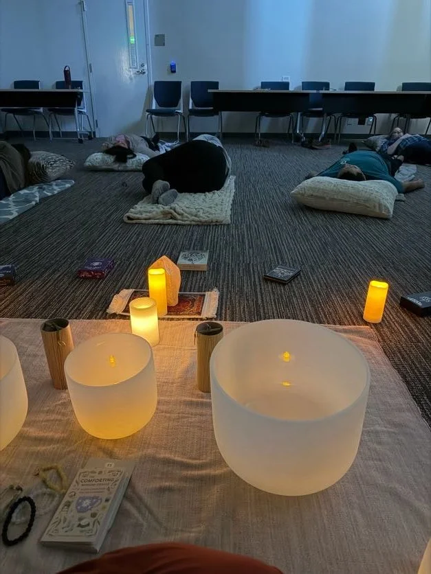 People lying down on cushions on a carpeted floor in a room, with candles and decorative objects in the foreground.