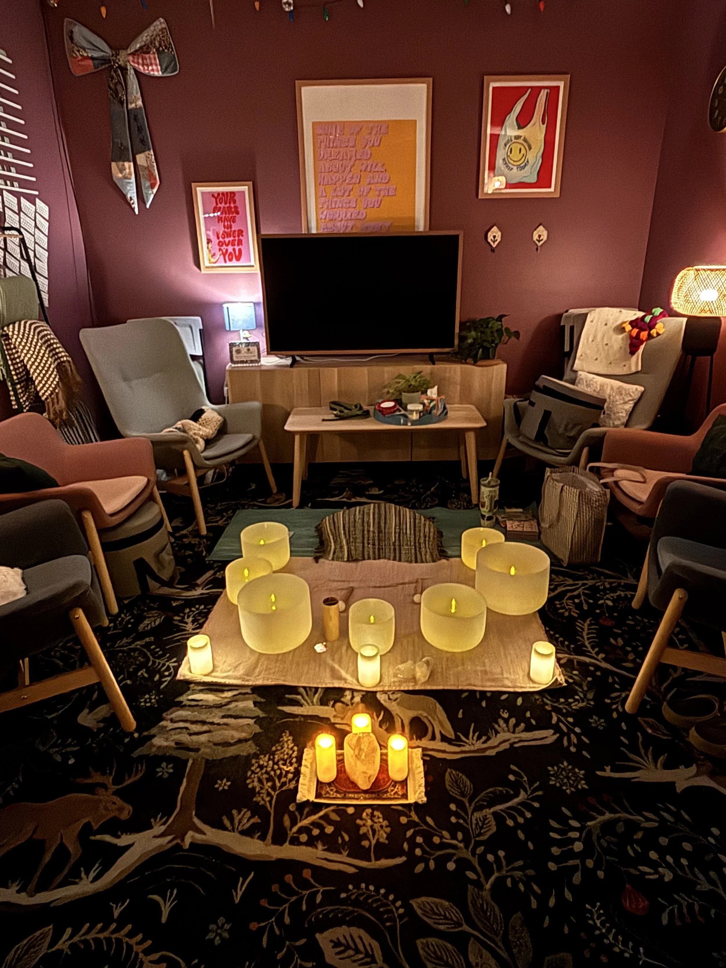 Living room decorated with numerous candles on the floor and a large sofa, chairs, and artwork on the walls.