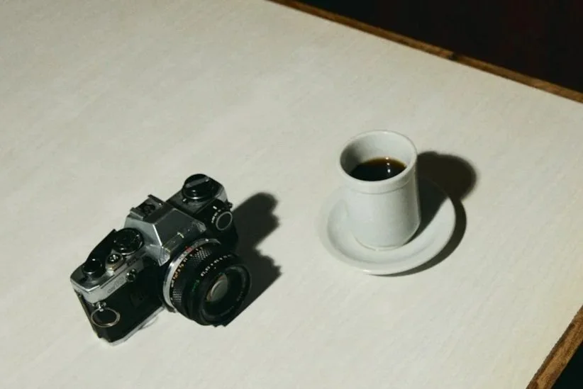 A vintage camera and a white cup of black coffee on a white table.
