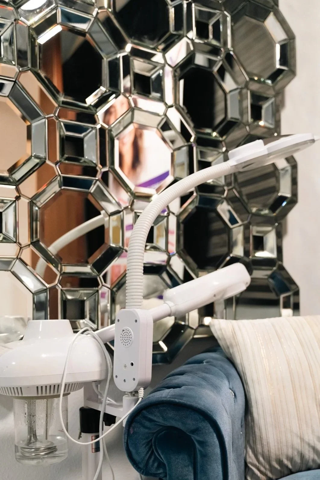 A decorative mirror with a hexagonal pattern above a close-up view of a robotic vacuum cleaner on a table, with a blue upholstered sofa and a cream-colored cushion in the background.