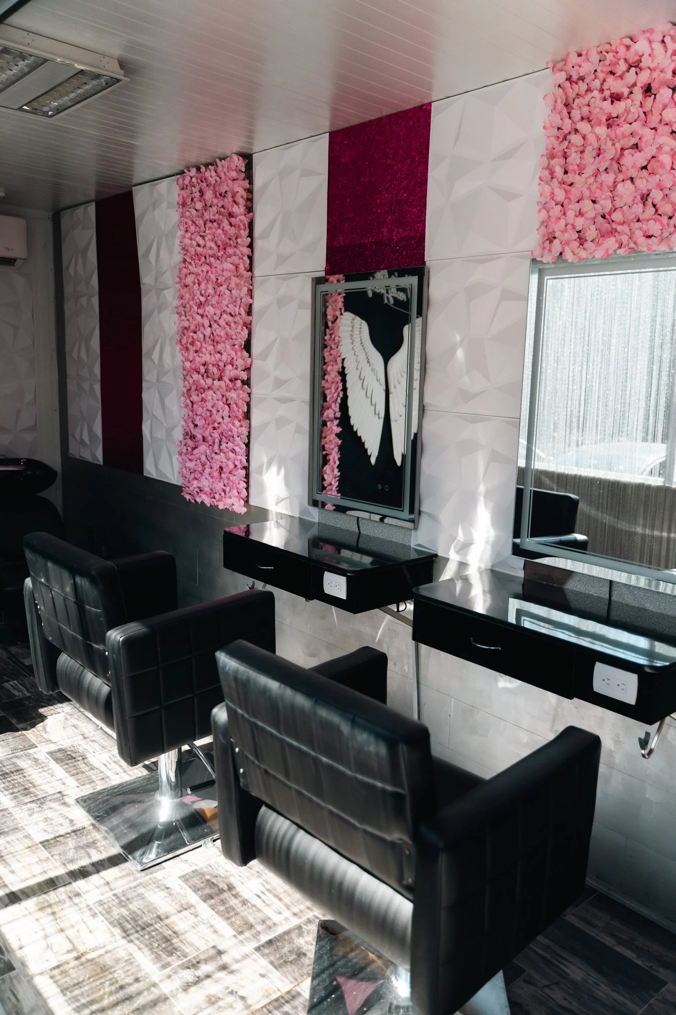 Indoor salon with black chairs, pink floral wall decorations, and a mirror with a black frame.