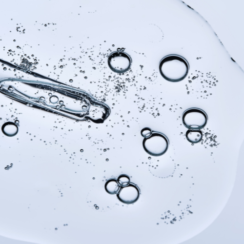 Microscopic view of water with bubbles and oil droplets in a clear liquid.