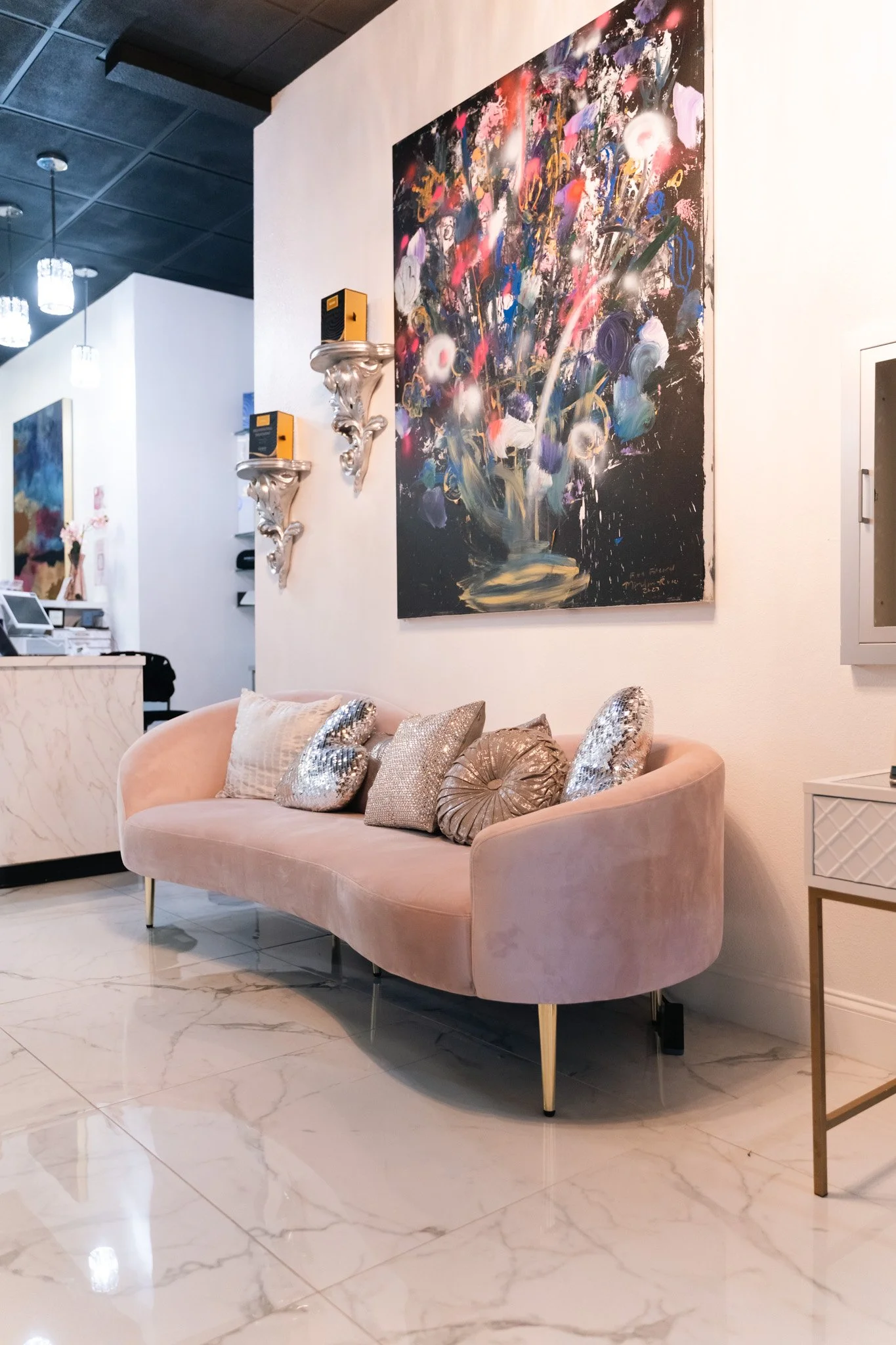 A pink velvet sofa with seven decorative pillows and a large abstract painting on the wall above it in an elegant interior space.