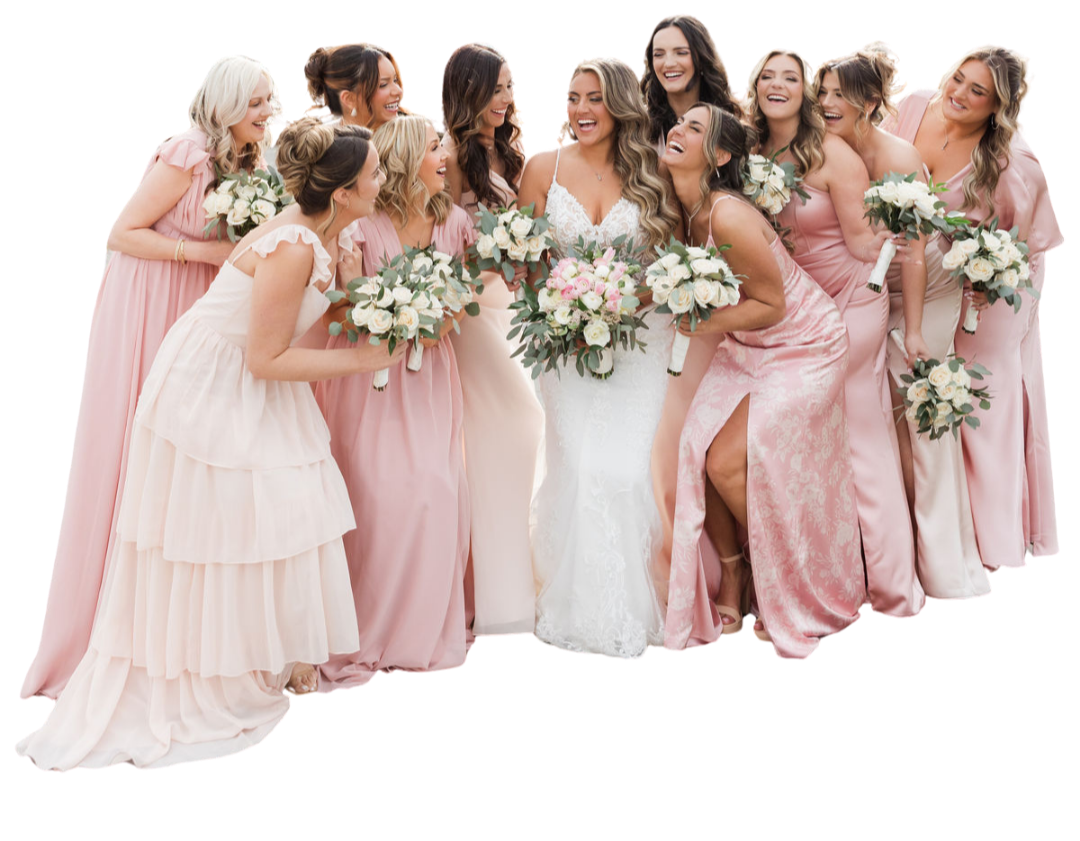 A bride in a white wedding dress surrounded by her bridesmaids in pink dresses, all holding bouquets of flowers, smiling and celebrating.