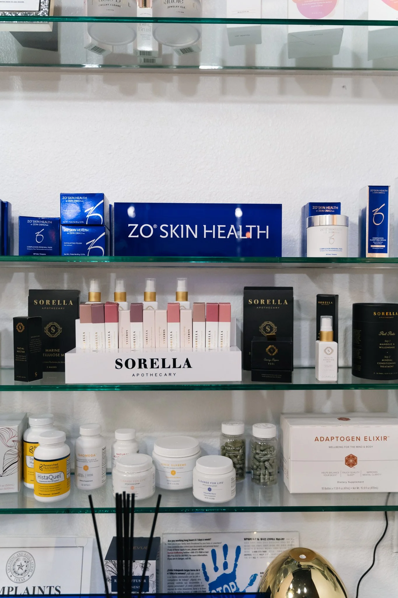Display of skincare products at a store, including ZO Skin Health, Sorella Apothecary, and dietary supplements, with a glass shelf above.