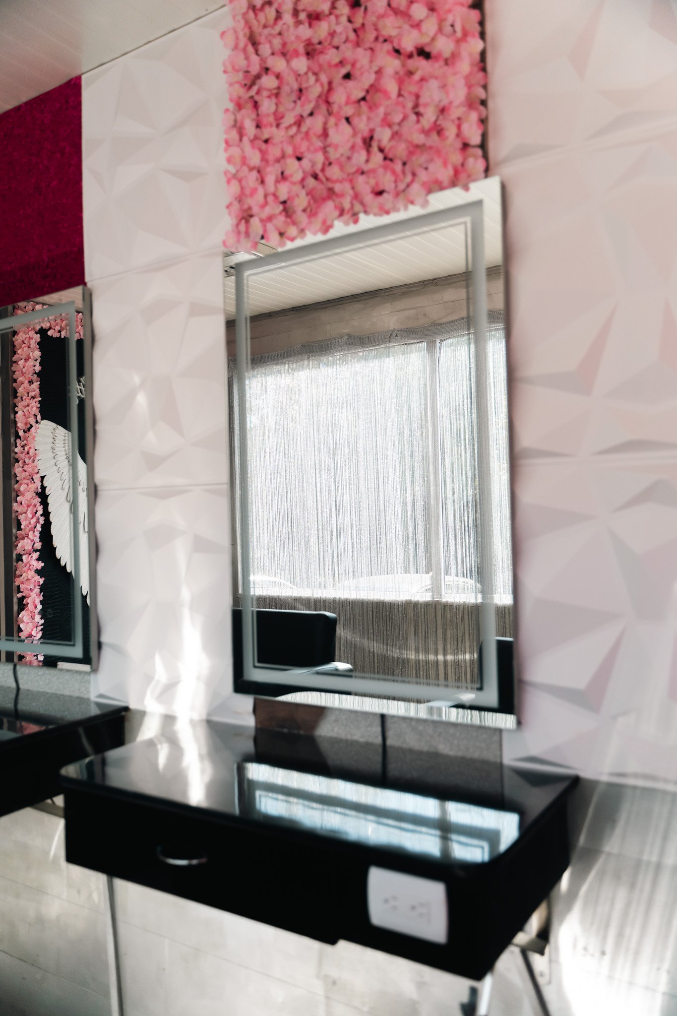 Modern black vanity with a mirror, set against pink and white textured walls, with a large window with curtains in the background.