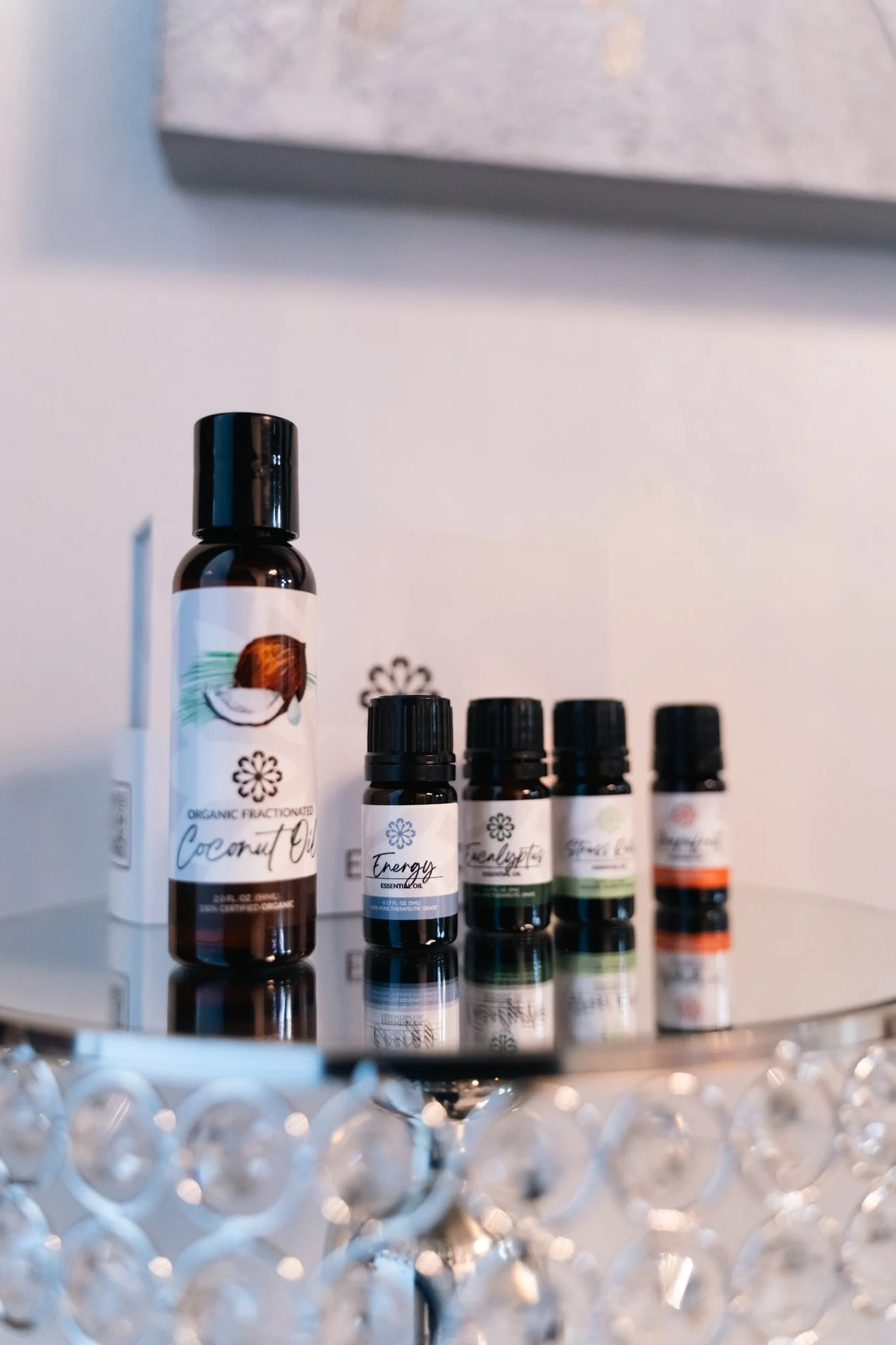 Collection of essential oil bottles placed on a mirrored surface with a decorative crystal stand below.