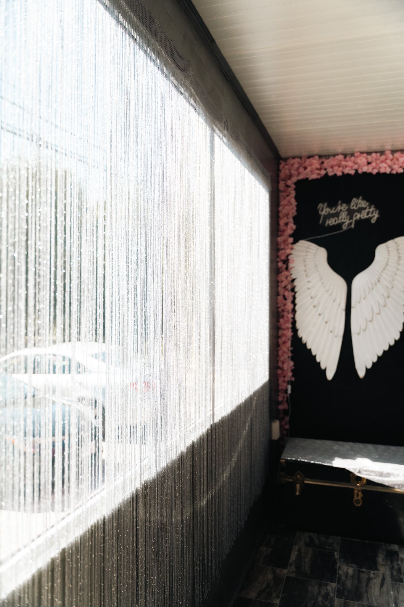 Indoor space with a window curtain partially open and a decorative wall with angel wings and pink floral border.