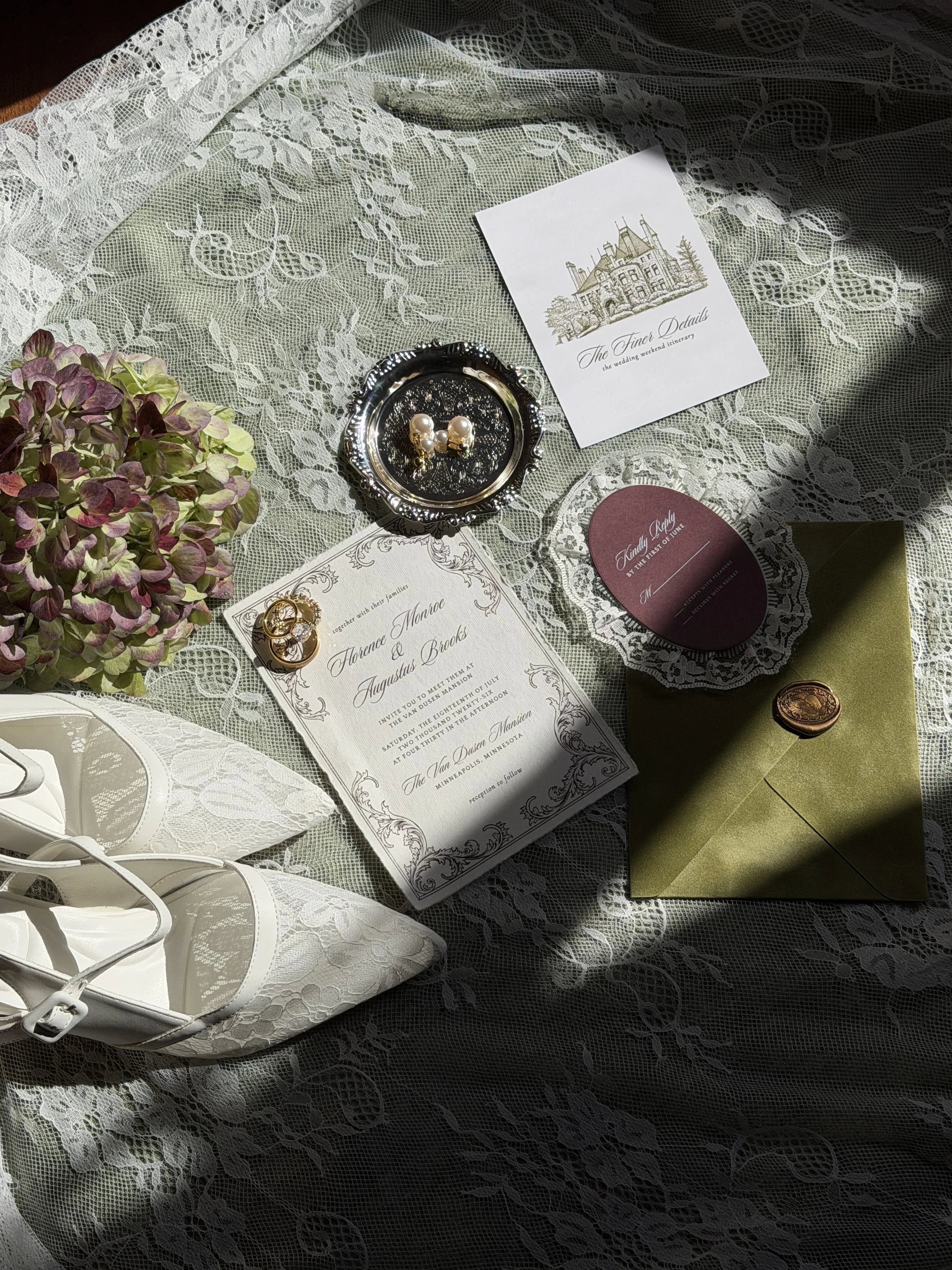 A lace tablecloth with wedding invitations, jewelry, an envelope with a wax seal, a pair of pearl earrings, and a floral arrangement.
