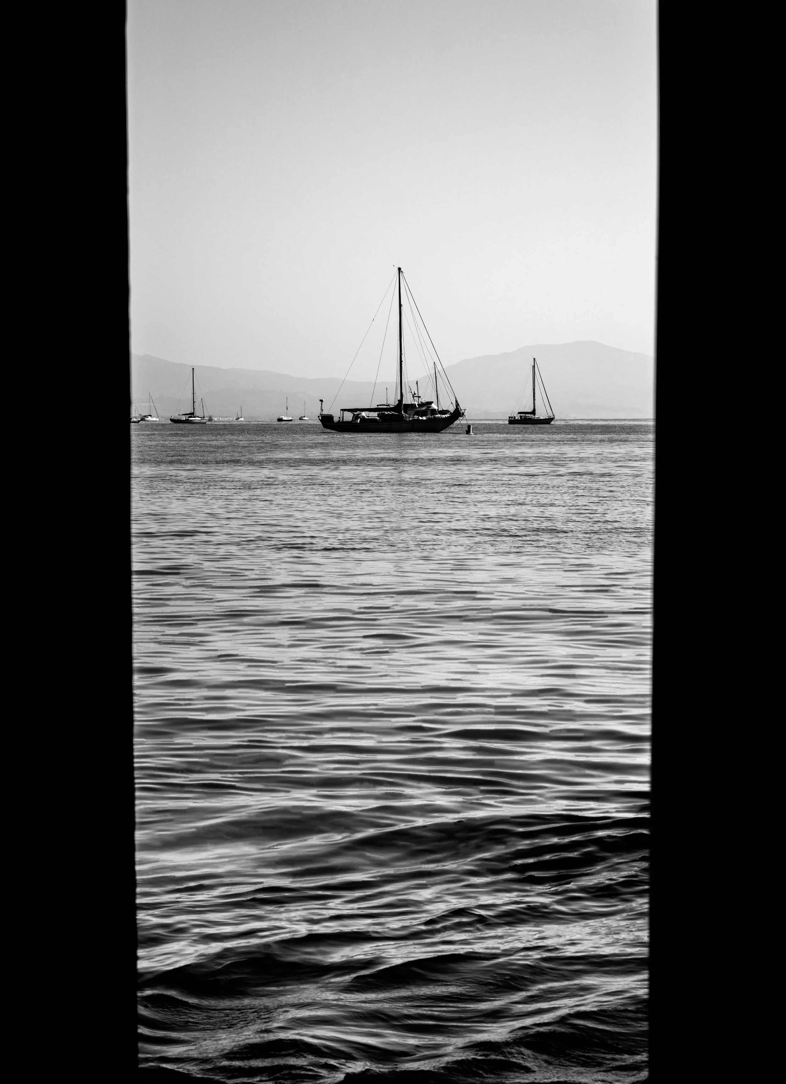 Black and white photo of a boat at sea in a body of water with mountains in the background