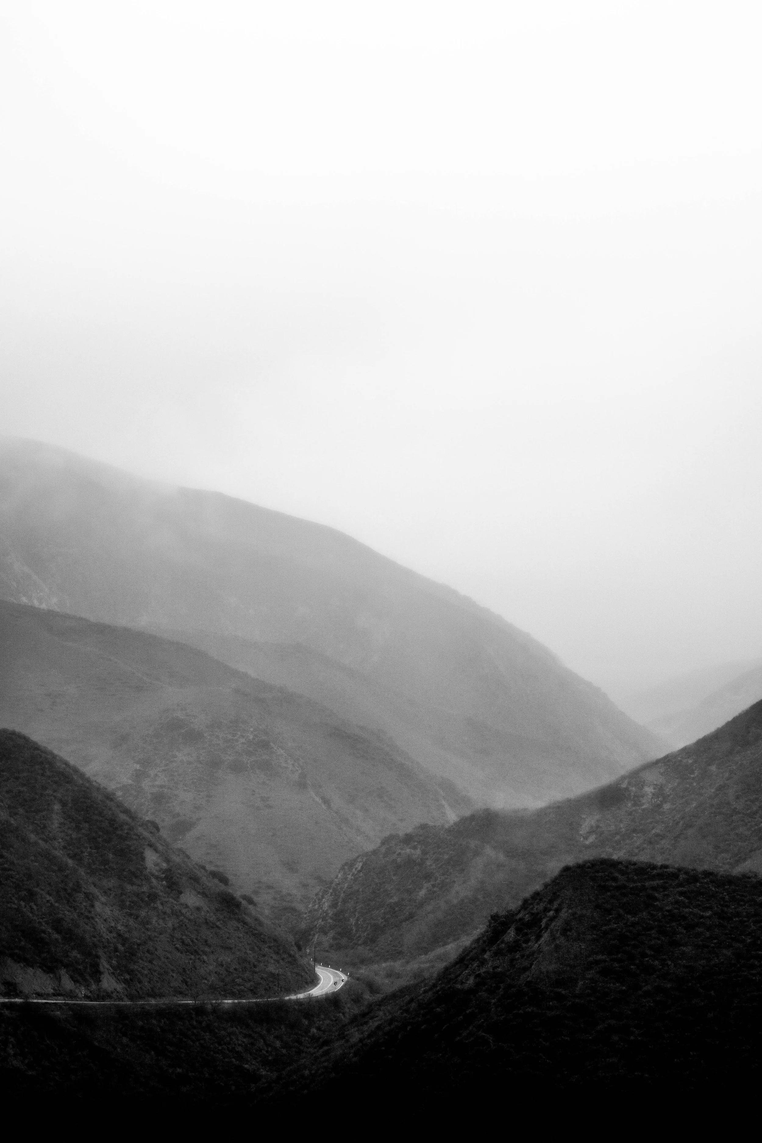 Black and white photograph of foggy mountain landscape with a winding road in the valley.