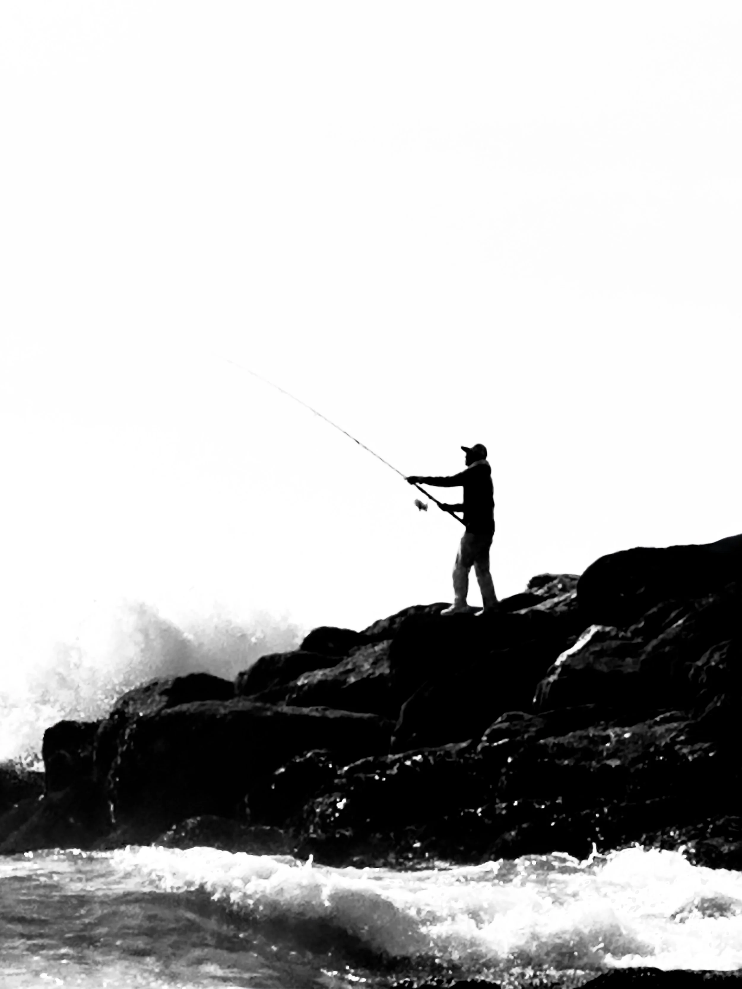Silhouette of a person fishing on rocks near water.
