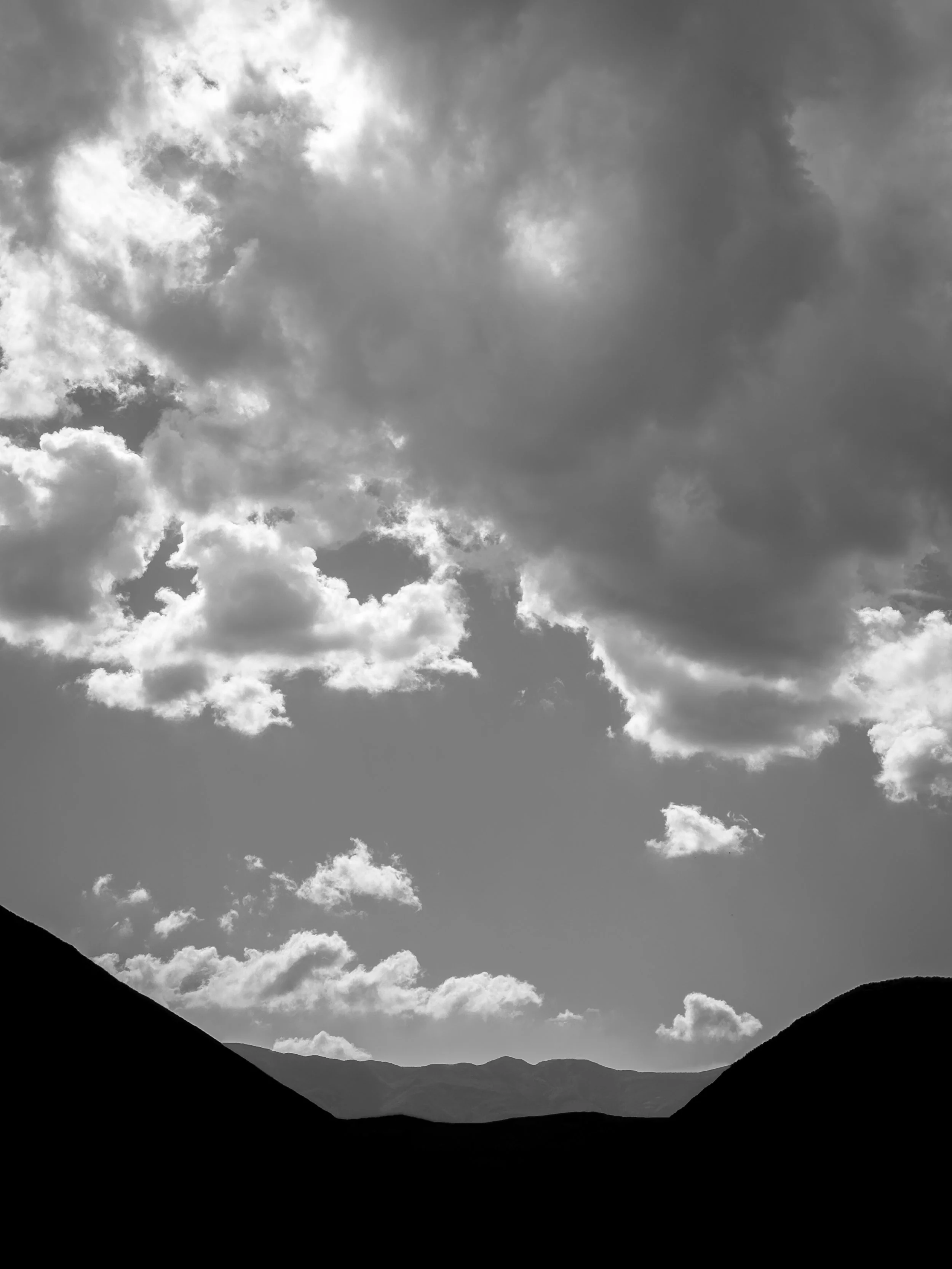 Black and white photo of a cloudy sky over mountain ridges.