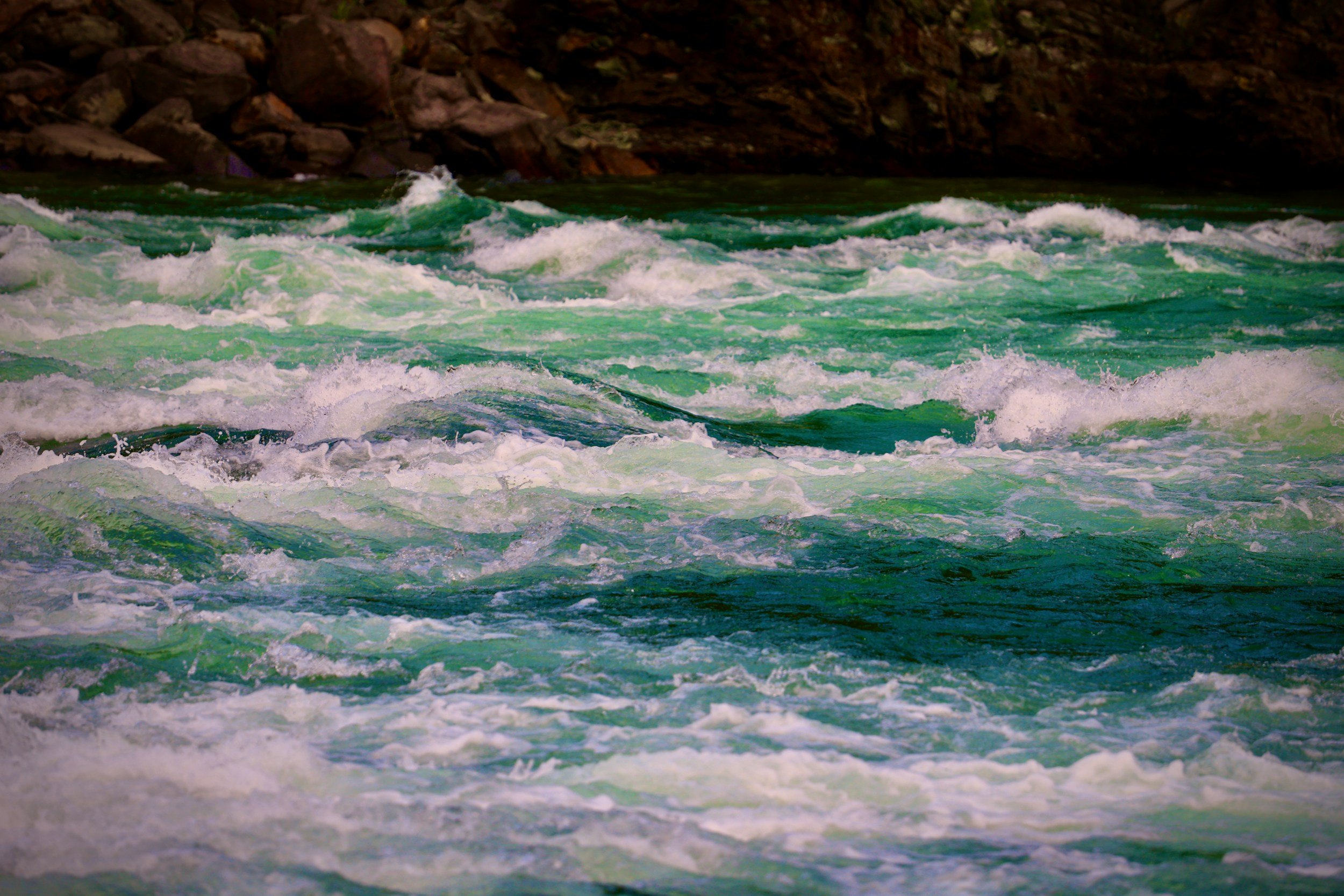 Green and white water rapids with rocks in the background.