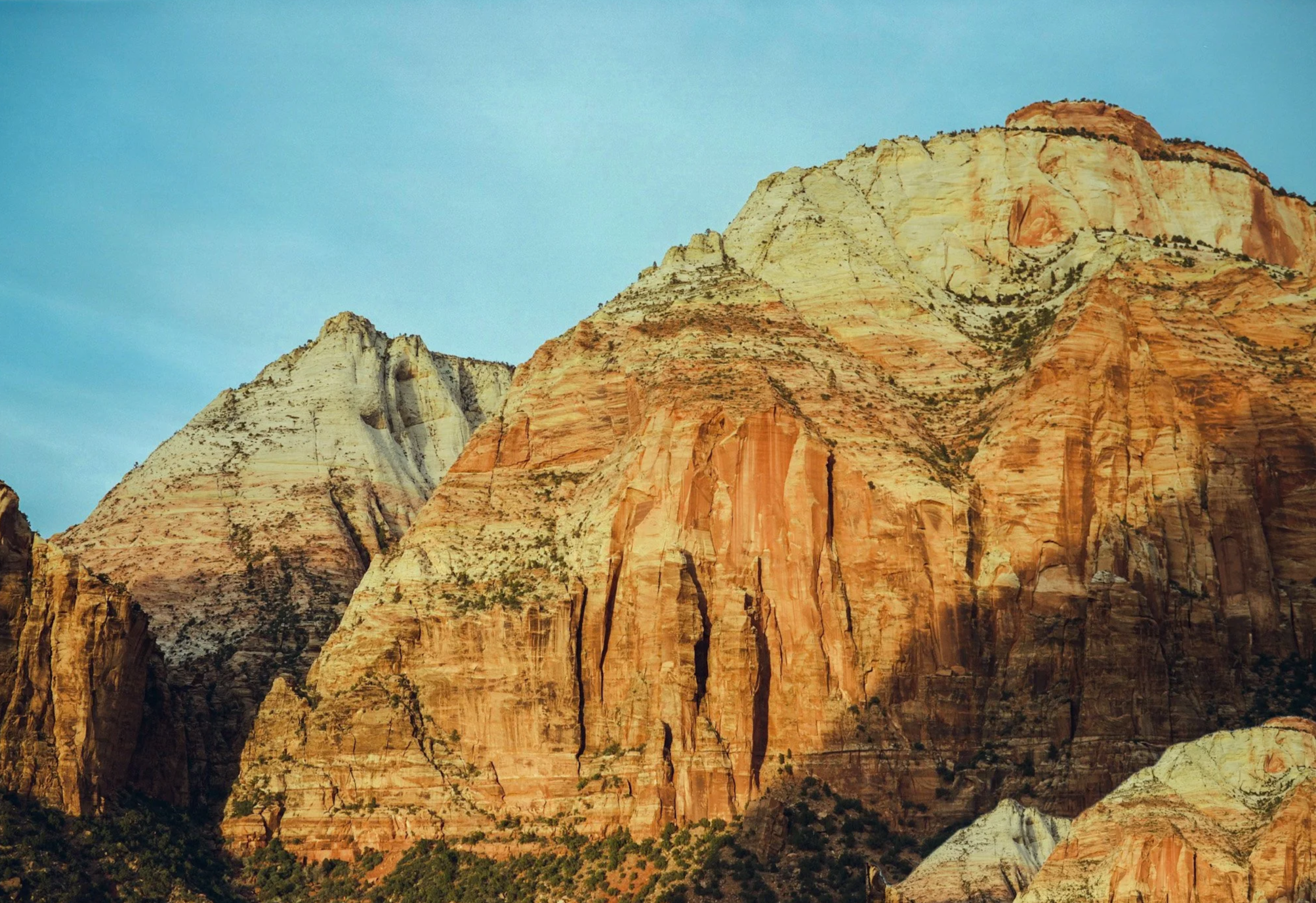 Colorful desert mountains with layered rocks in shades of red, orange, yellow, and white under a clear blue sky.