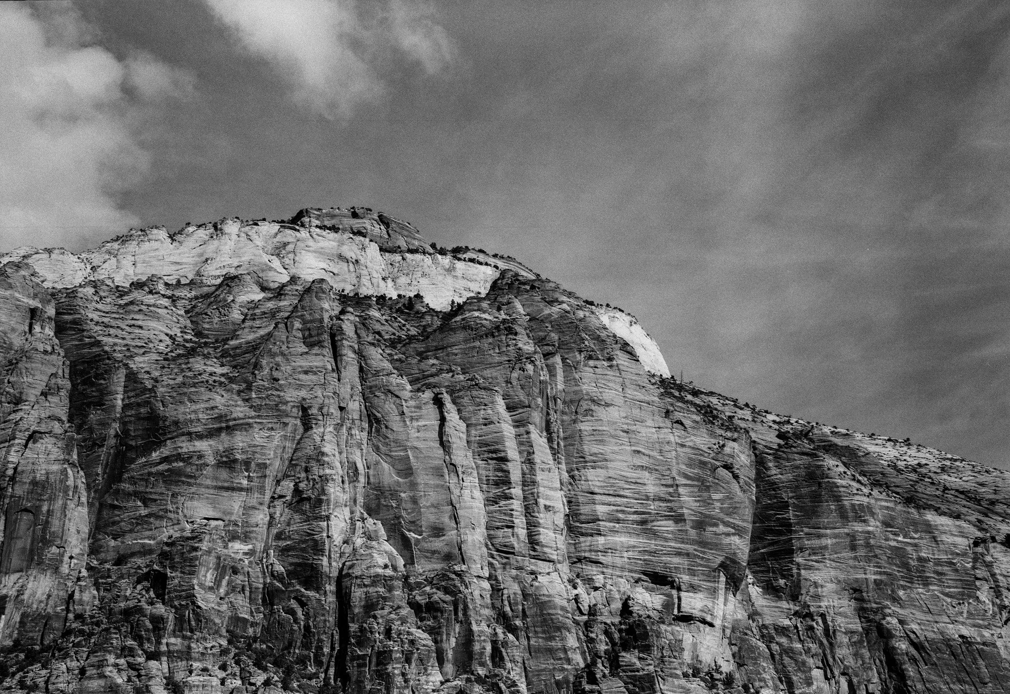 Black and white photograph of a rugged mountain with steep cliffs, layered rock formations, and sparse vegetation.