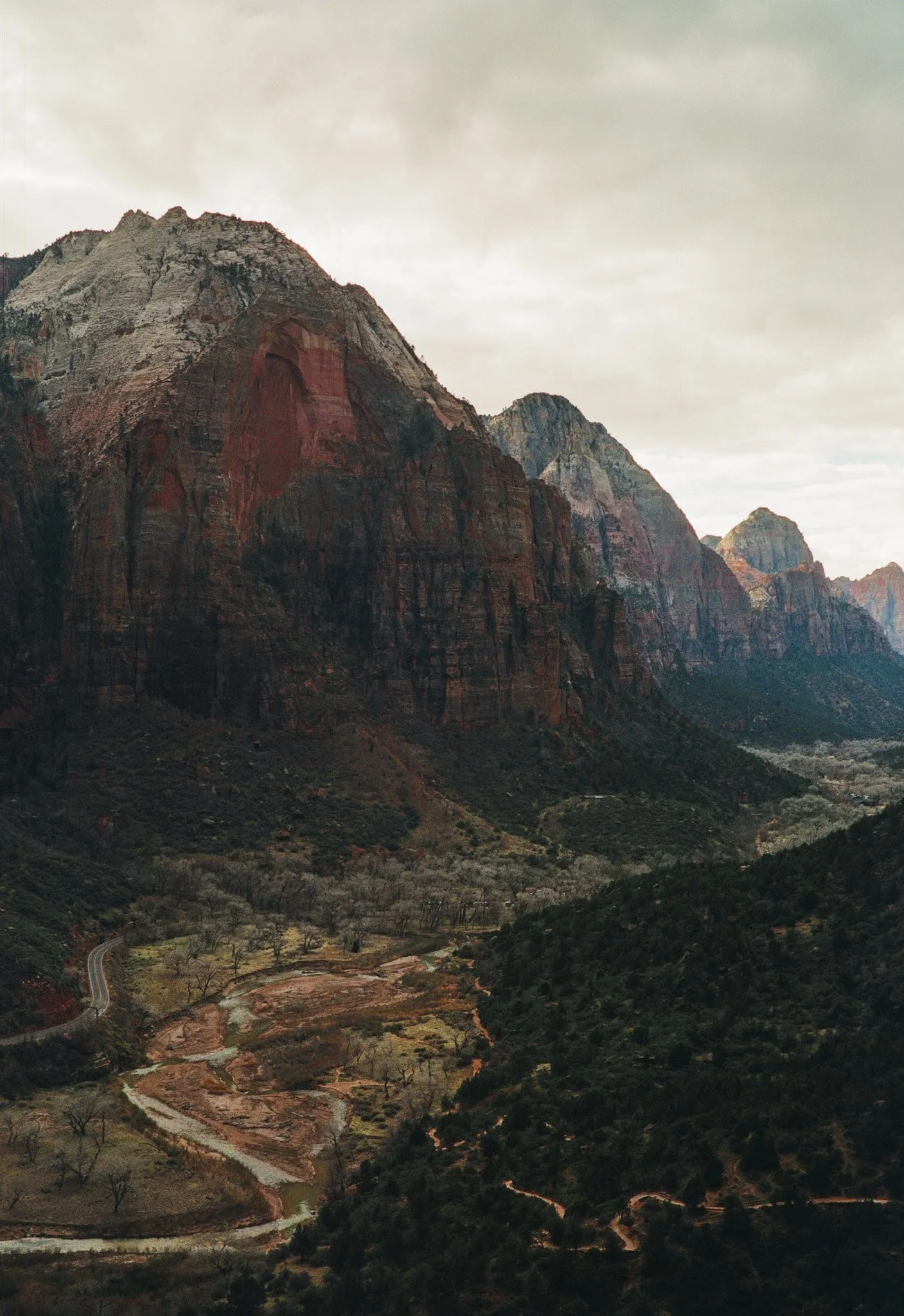 Scenic view of a mountainous canyon landscape with steep cliffs, winding river, and sparse trees under a cloudy sky.