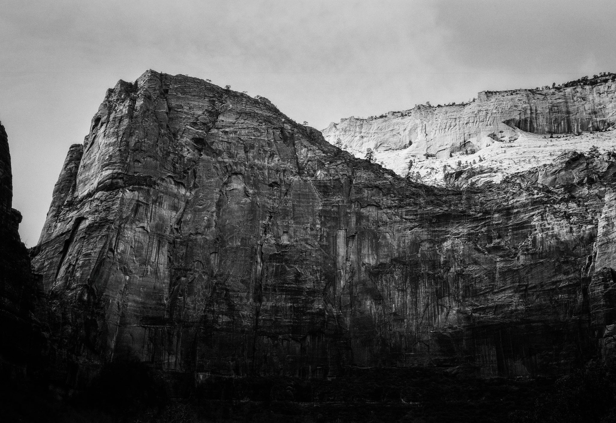 Black and white photo of a large mountain cliff with multiple layers and textures, with some snow on top.
