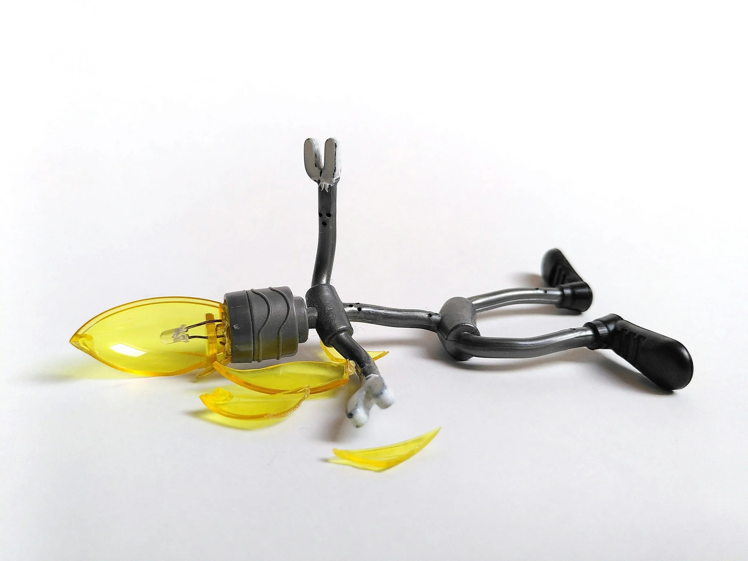 A lamp socket with a yellow teardrop bulb into the socket as a neck and a stick figure body. The stick figure is laying down with a shattered bulb as the head.