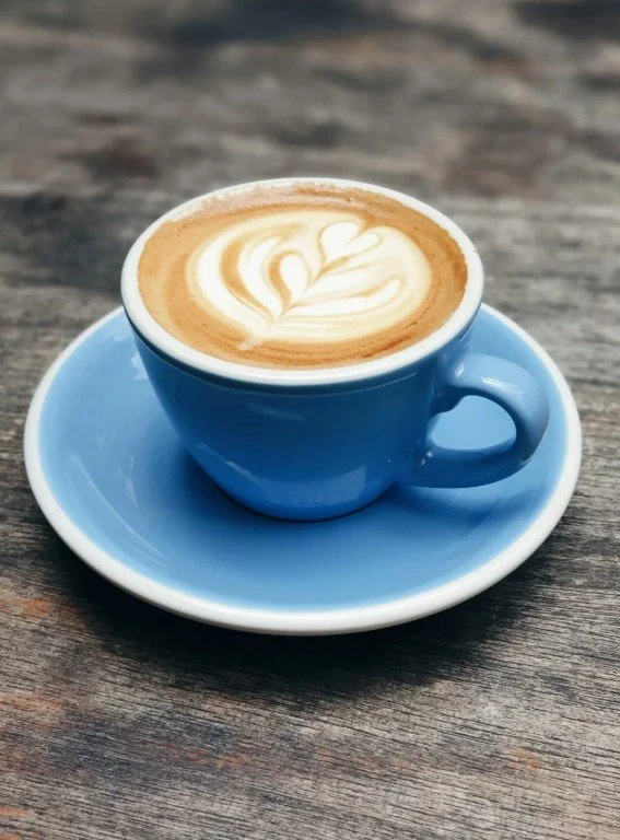 light blue coffe cup in a saucer filled with expresso and a leafy design in the froth.