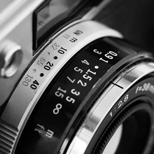 Close-up of a vintage camera lens with focus and aperture rings, showing various settings.