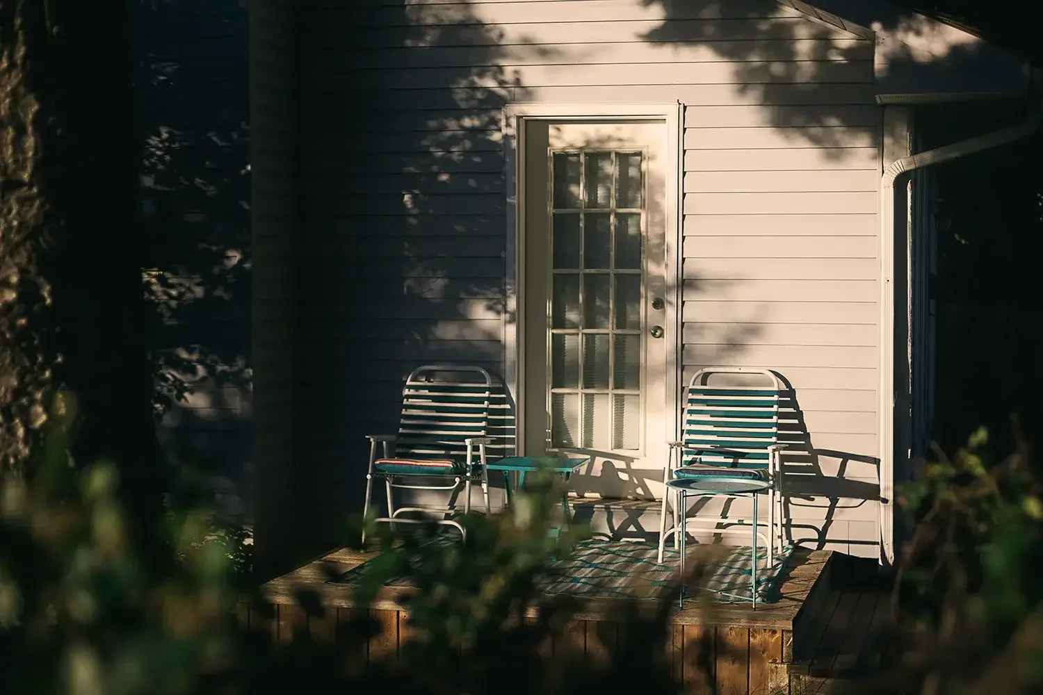 Two empty deckchairs in a sunny spot on decking surrounded by garden foliage