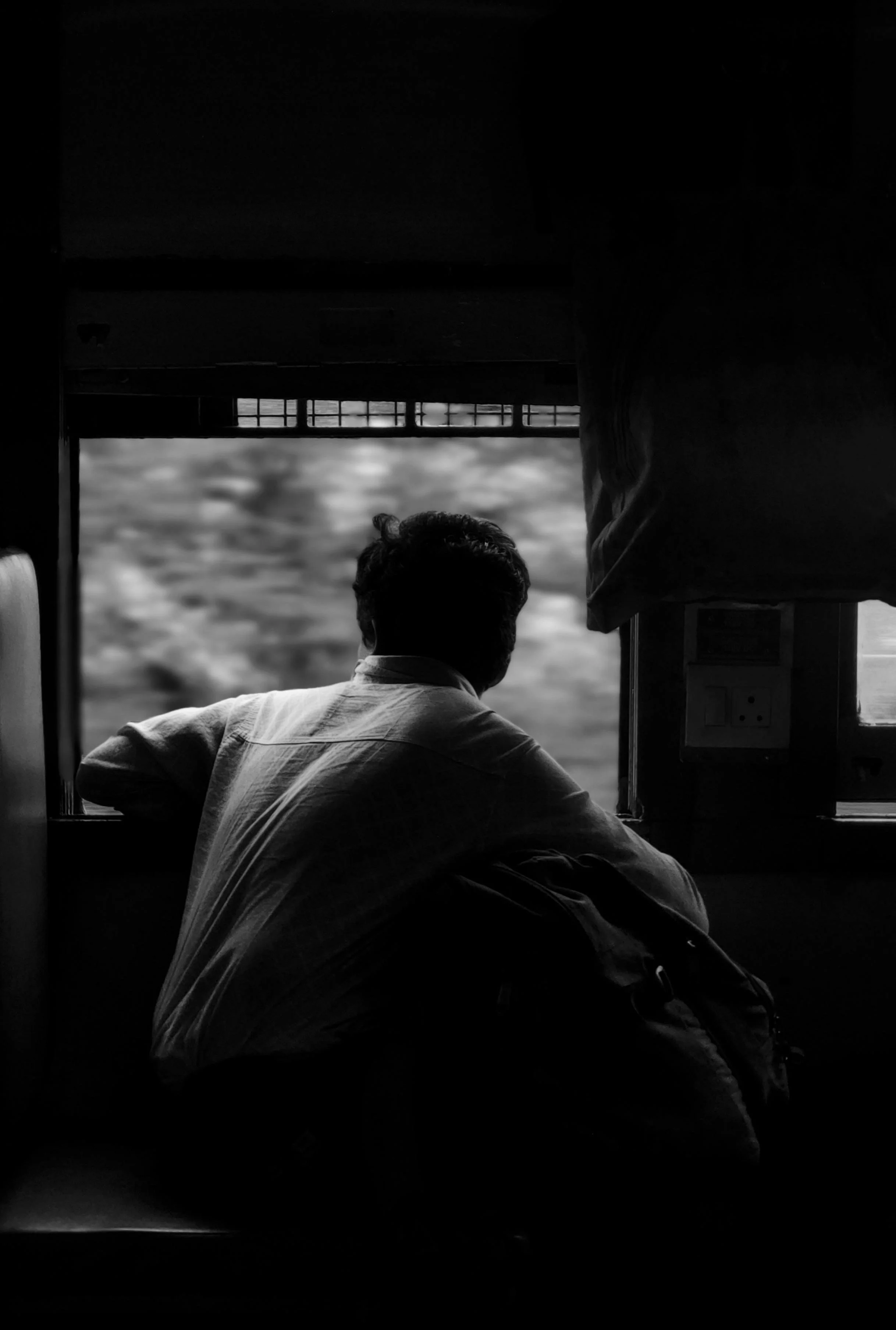 A man leaning on a window sill looking outside, silhouette in black and white.