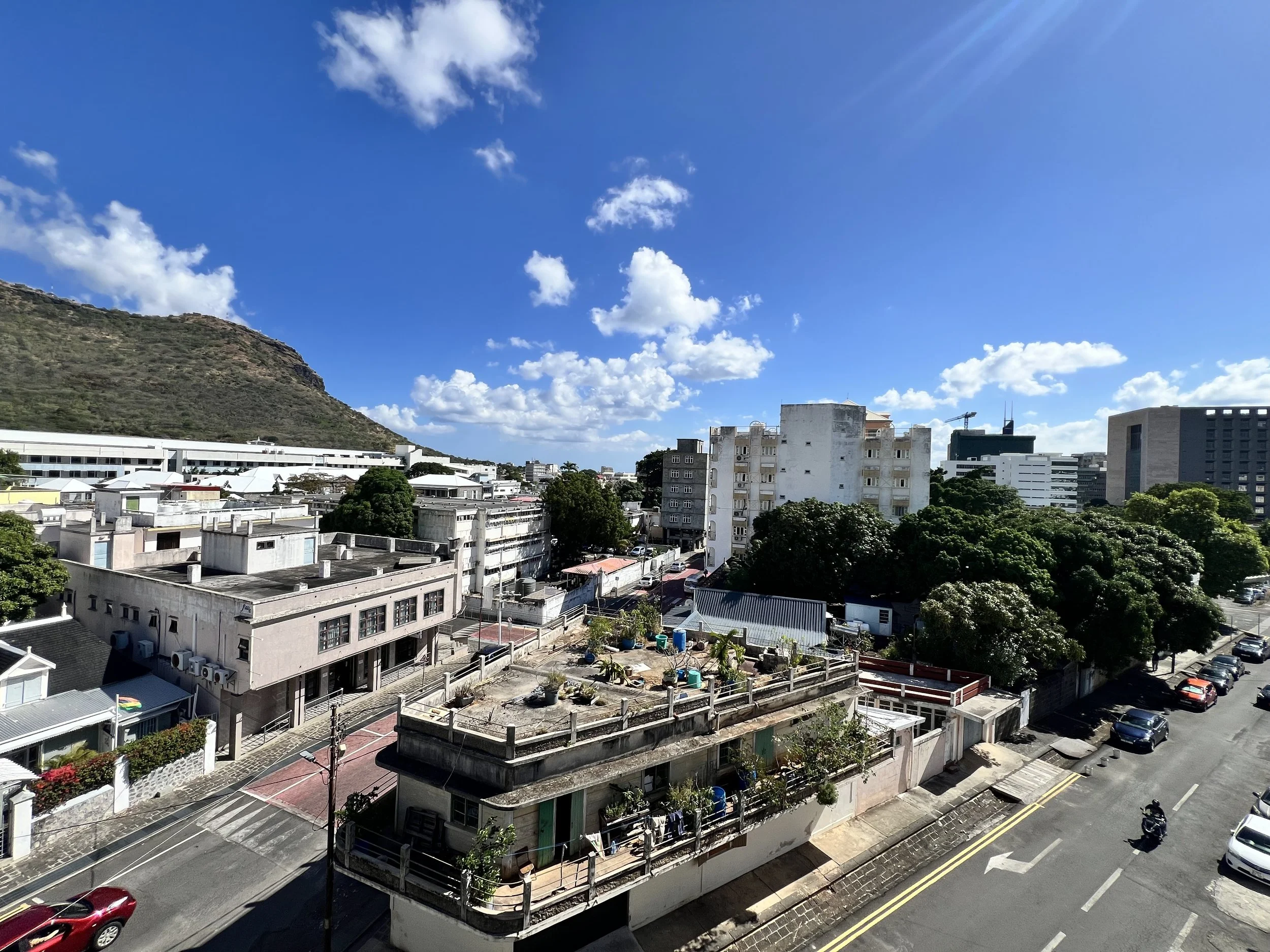 Cityscape with mid-rise buildings, a hill on the left, and a partly cloudy blue sky