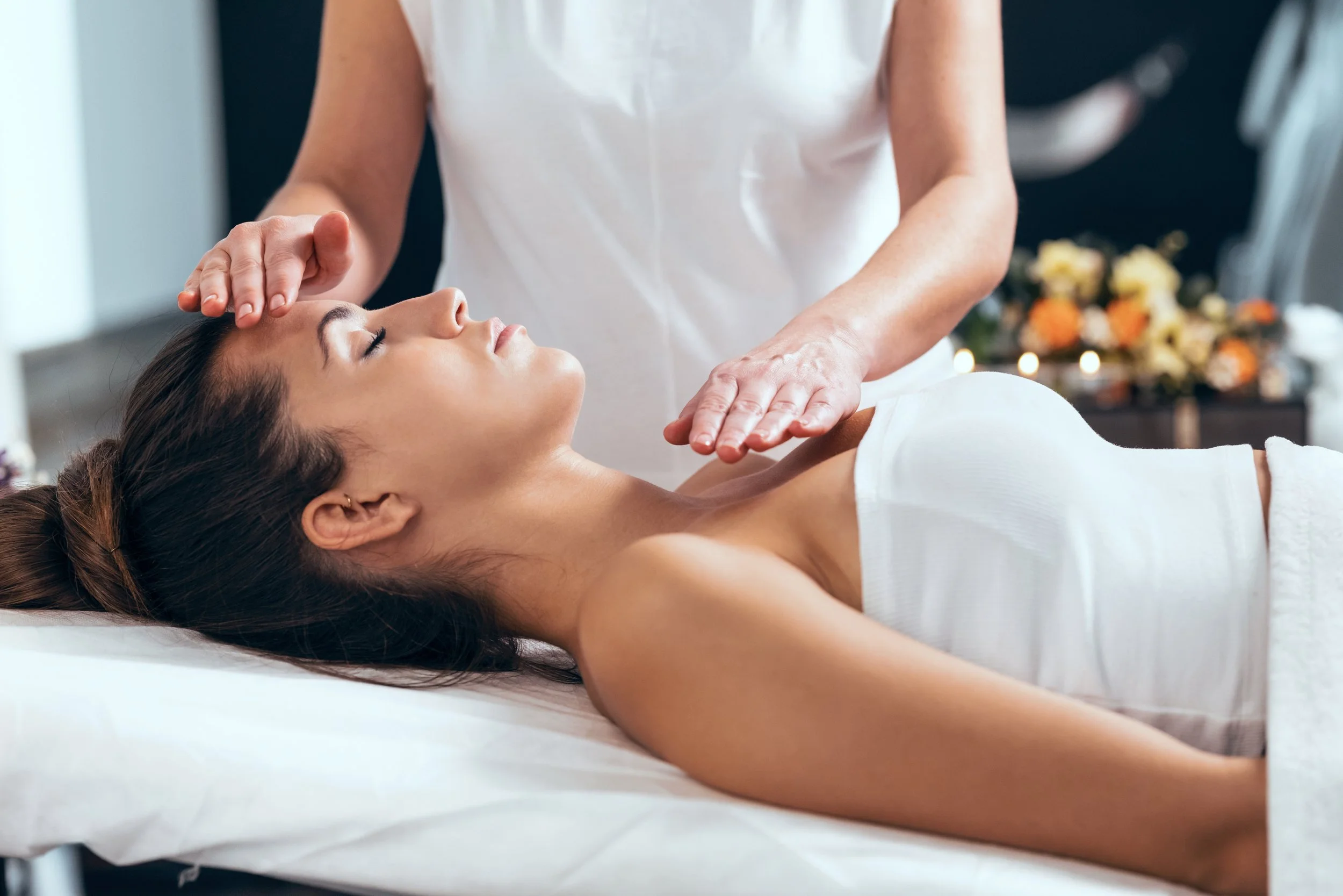 Woman receiving a facial massage at a spa, lying on a treatment bed with her eyes closed.