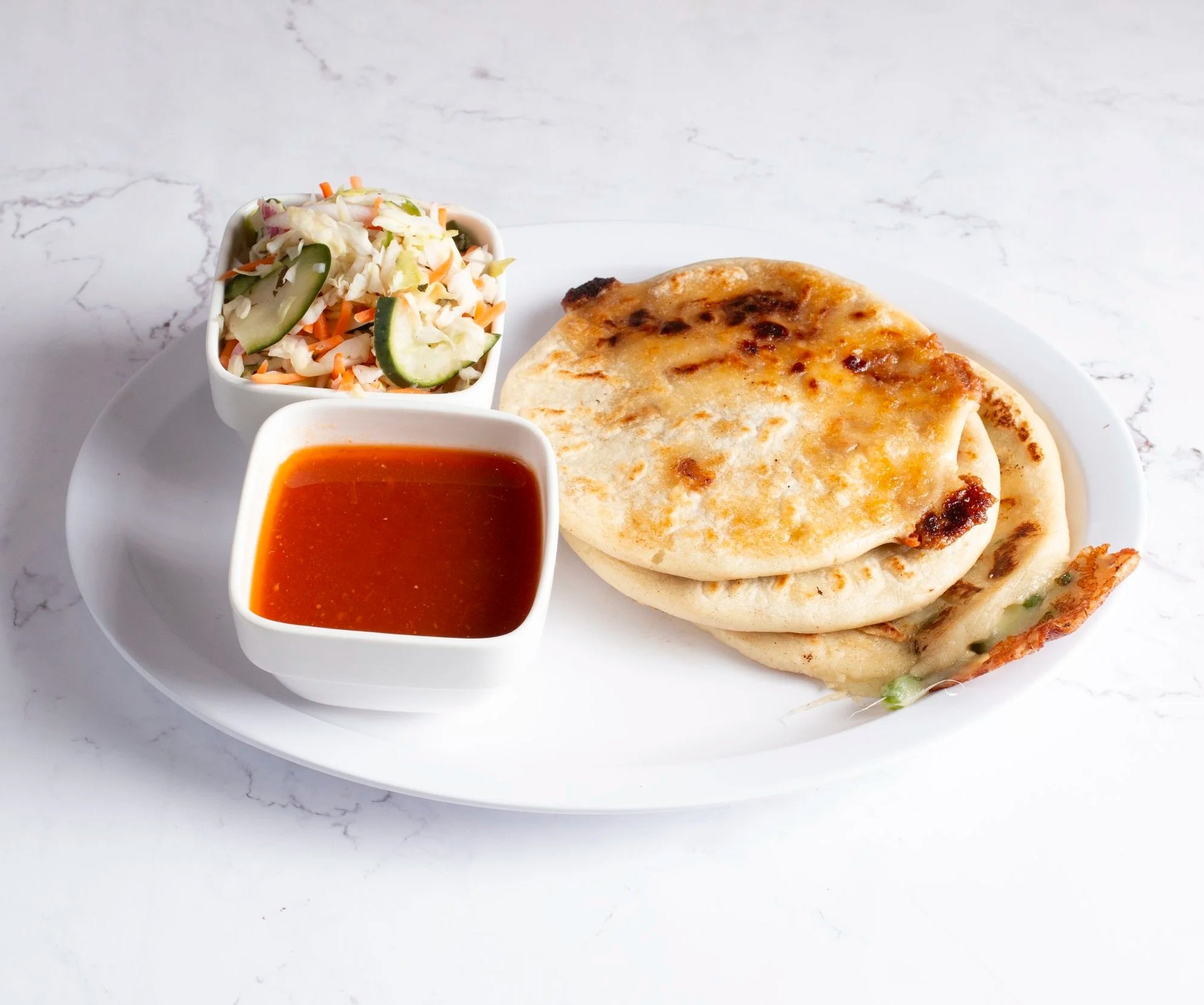 3 pupusas in a plate with curtido and homemade tomato sauce