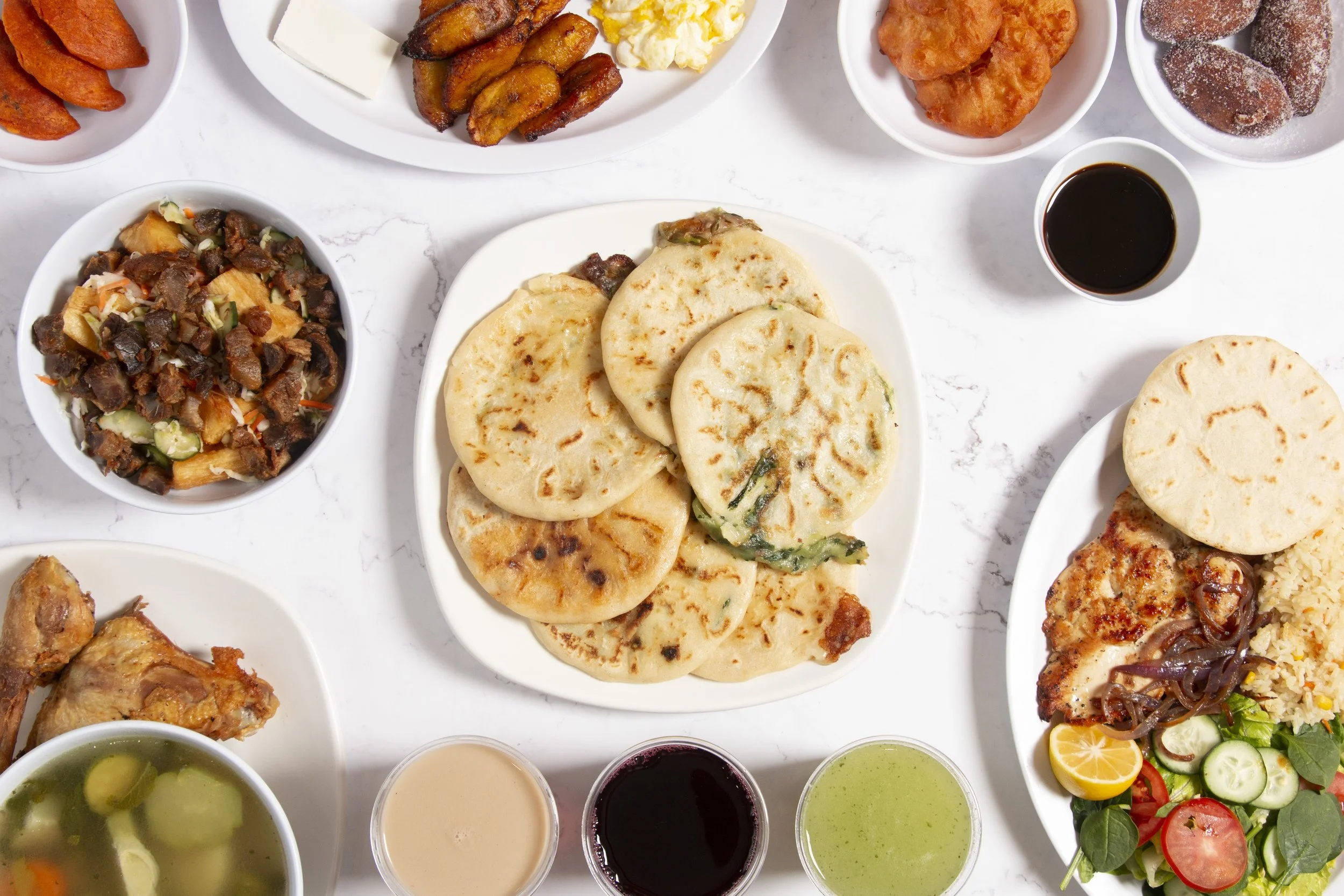 Pupusas and salvadoran food dishes layed out over a white marble table.