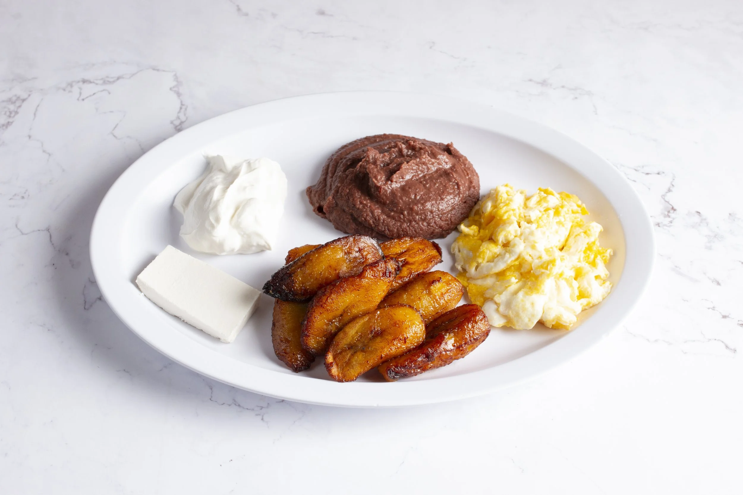 Salvadoran style breakfast with fried plantains, fried red beans, eggs, sour cream and queso fresco.