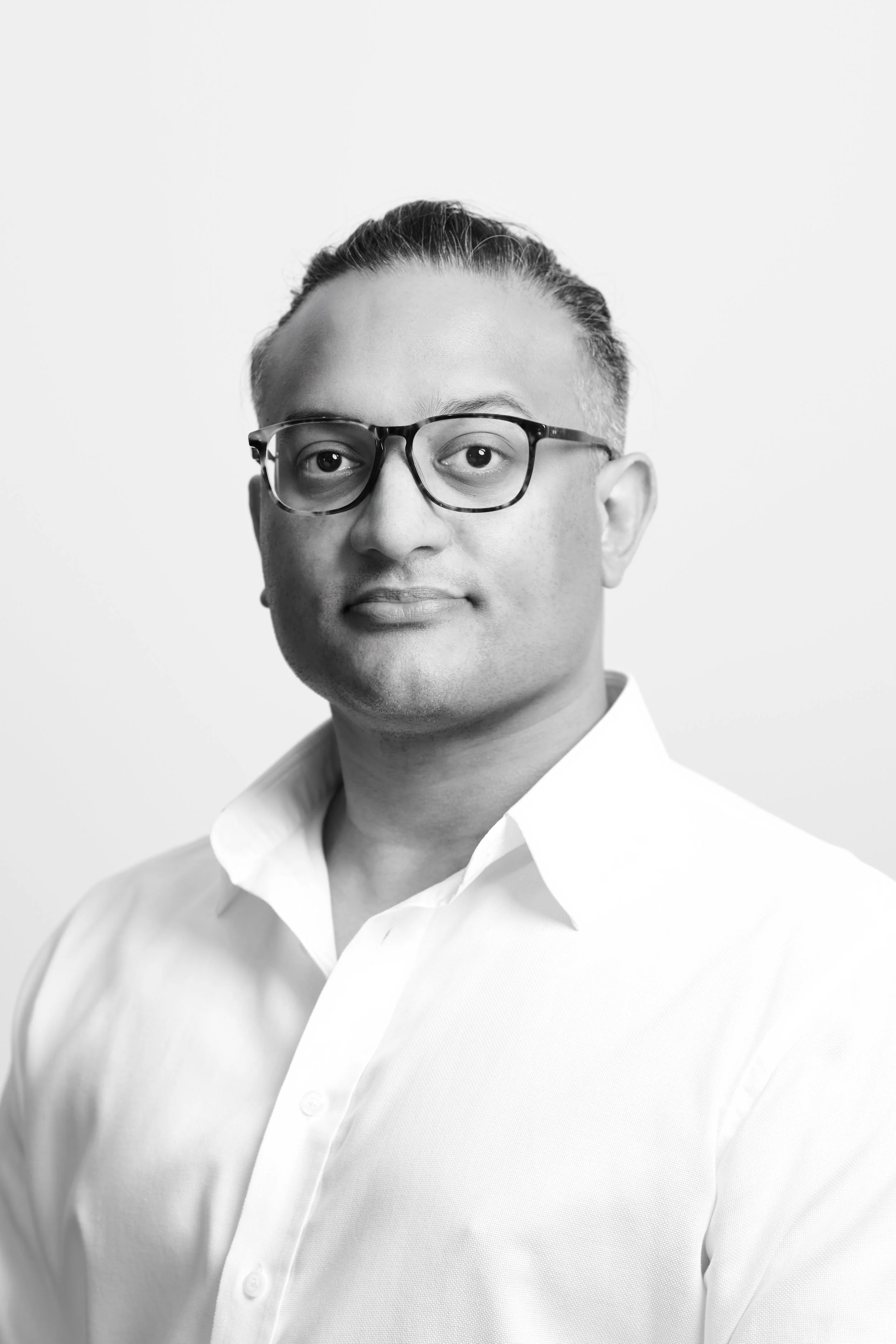 Black and white portrait of a man with glasses, short hair, and wearing a white shirt, against a plain light background.