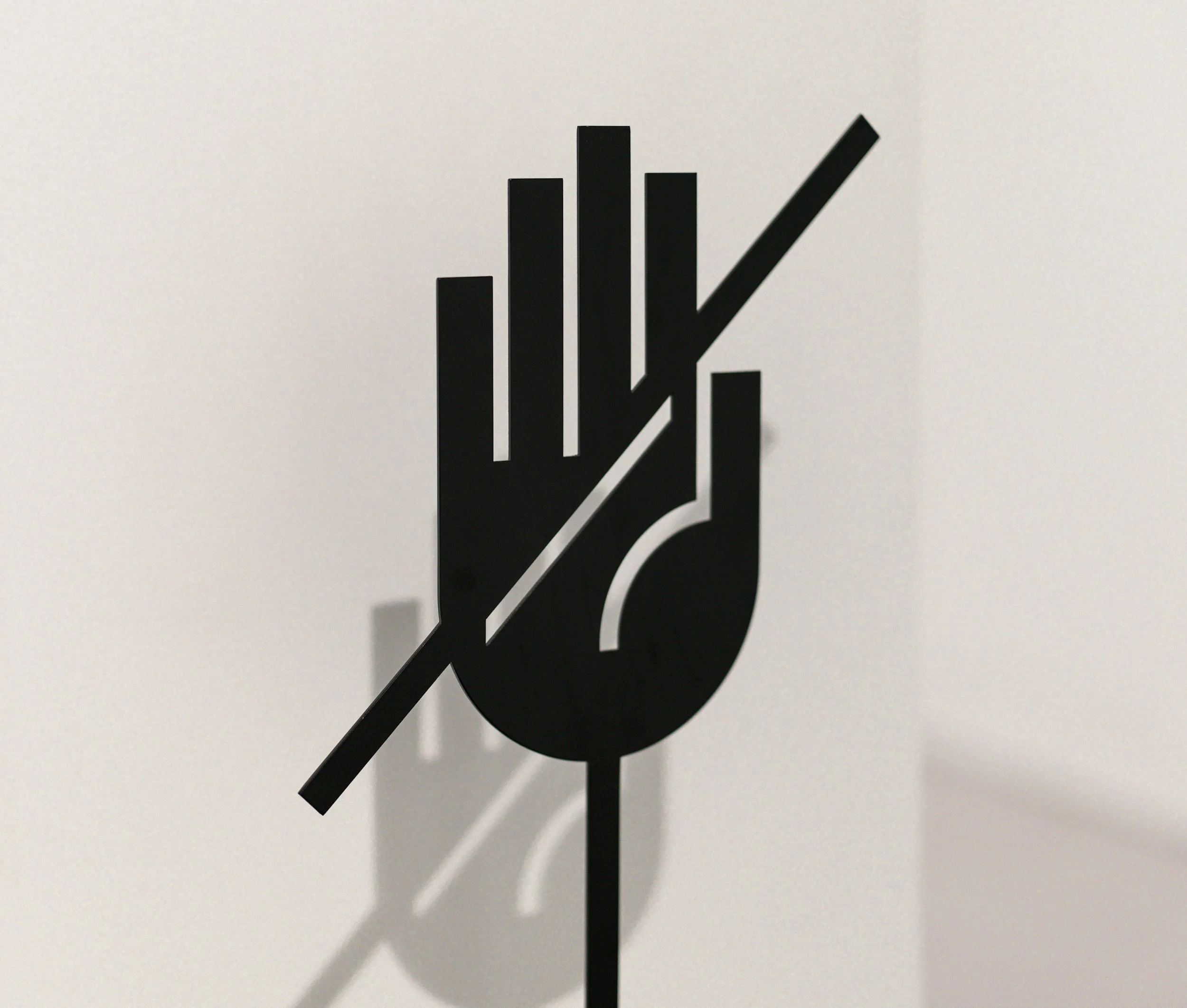 A black and white cutout of a hand holding a pen, with the pen pointing downward, casting a shadow on a light-colored surface.