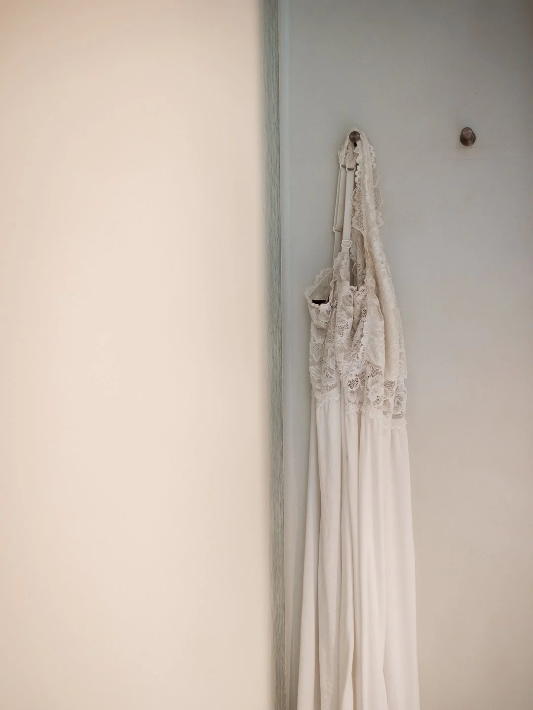 Witte laken met kant, hangend aan twee muurhaken op een witte muur.