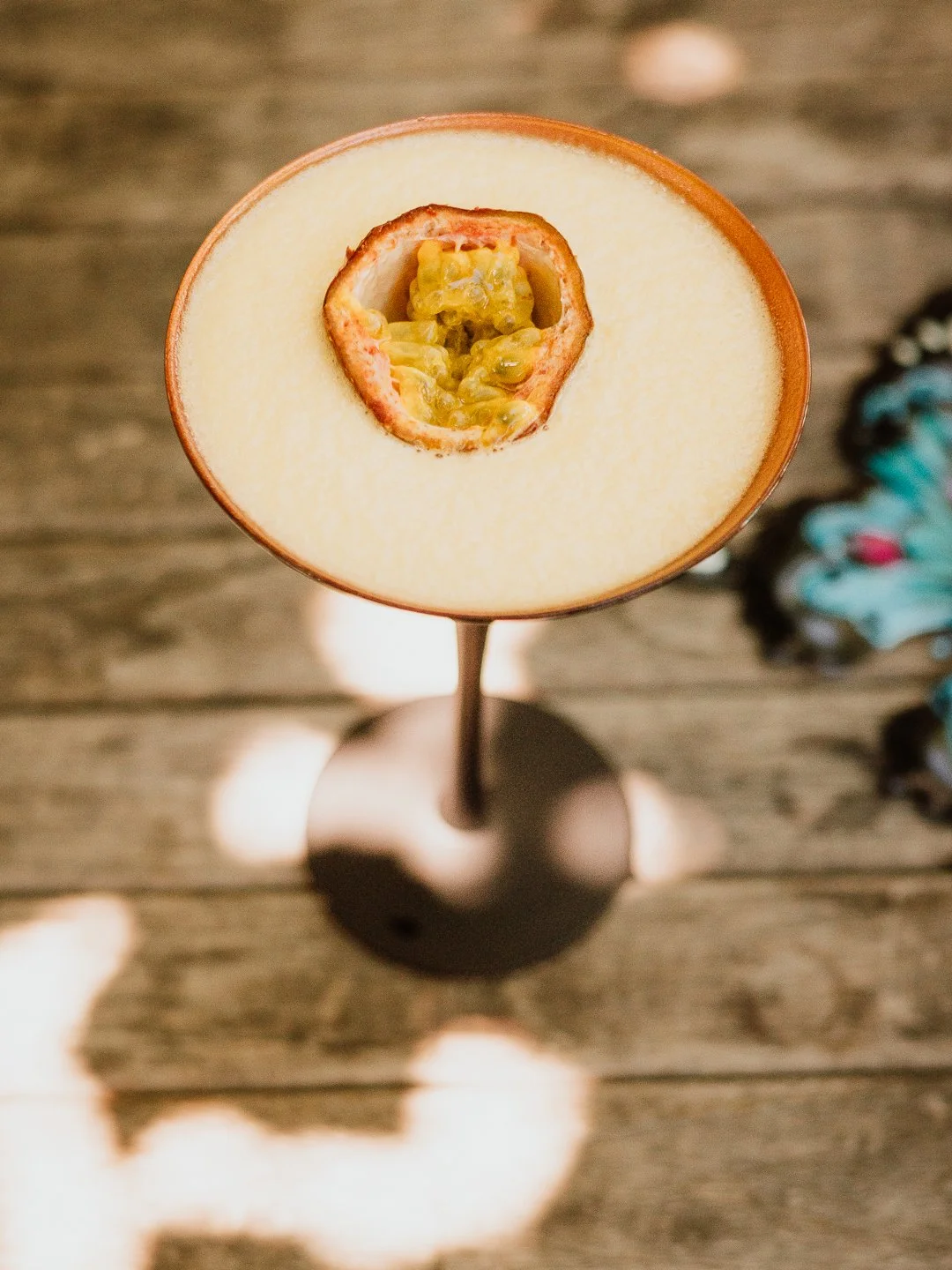 Een cocktailglas met een stevige bodem en een halfgelschaal op een houten tafel, gevuld met een geelachtig drankje en een gesneden passievrucht als garnering.