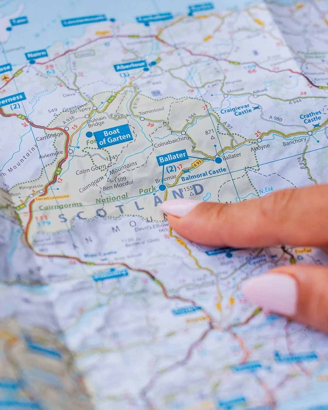 Close-up van een hand die op een kaart van Schotland wijst, met belangrijke locaties en routes zichtbaar.