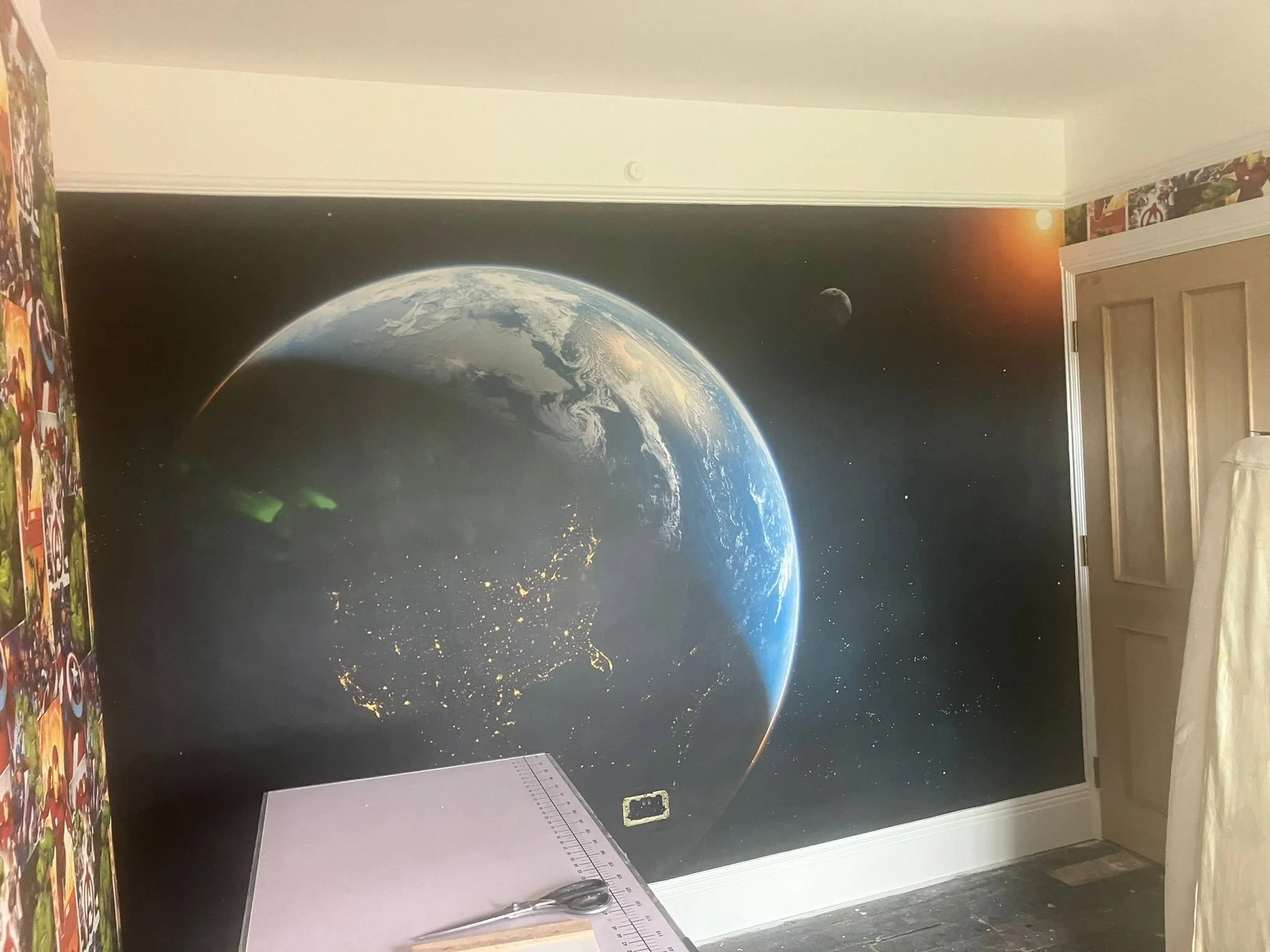 A wall mural of Earth seen from space, showing continents and city lights, with the moon and the sun in the background.