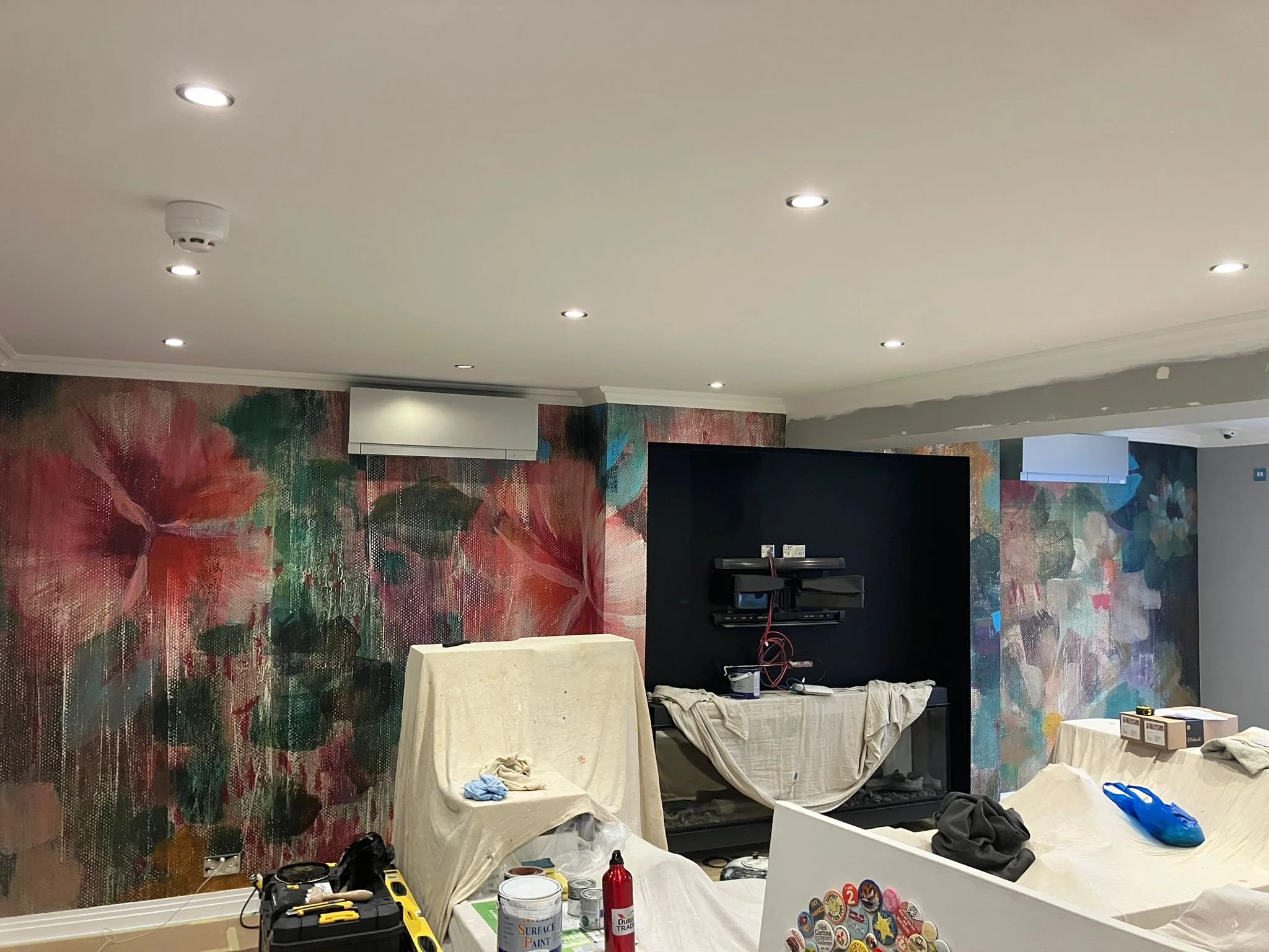 Living room with floral mural walls, ceiling lights, and a black entertainment center under construction with tools and supplies.